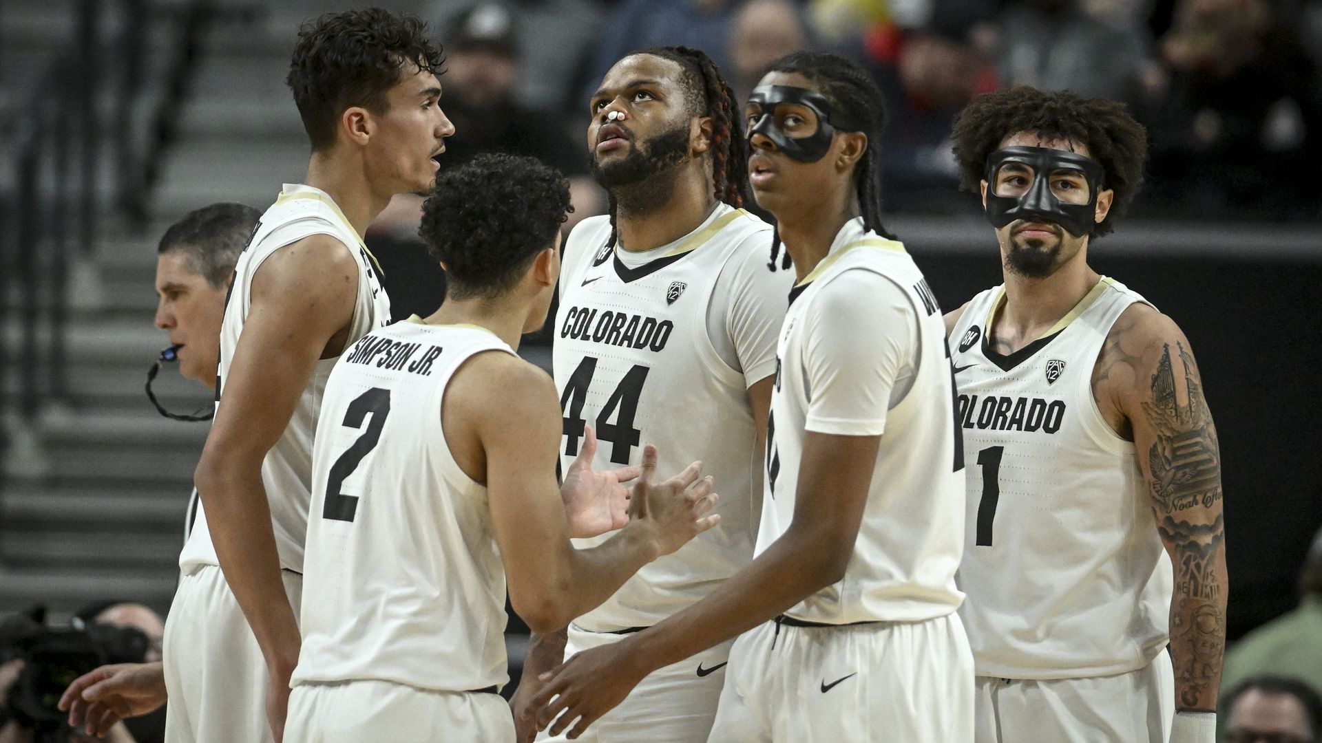 Several basketball players in white jerseys with the words COLORADO inscribed on the front stand close together during a game. 
