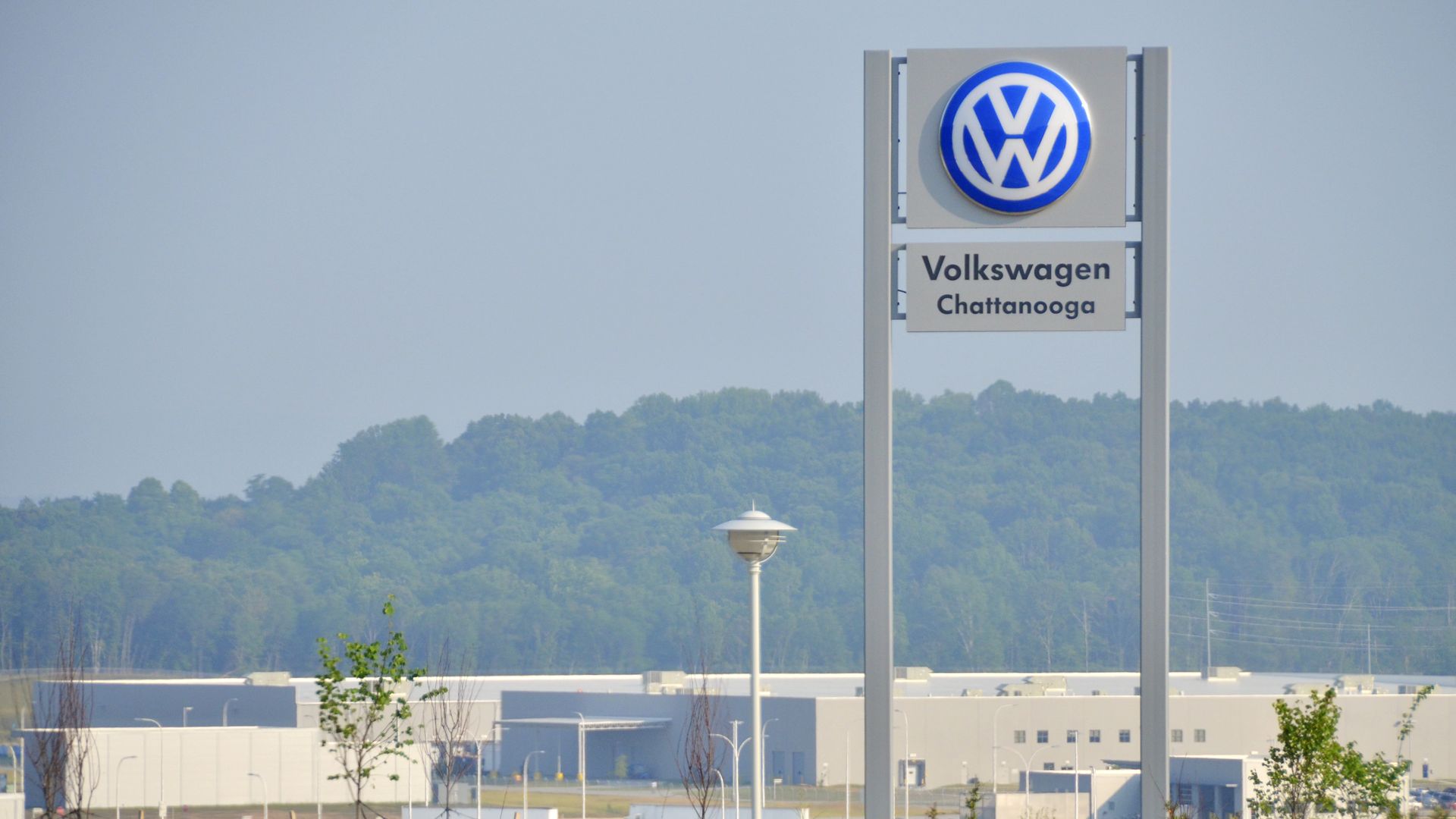 The logo of Volkswagen is perched high atop a metal sign, looming over a factory