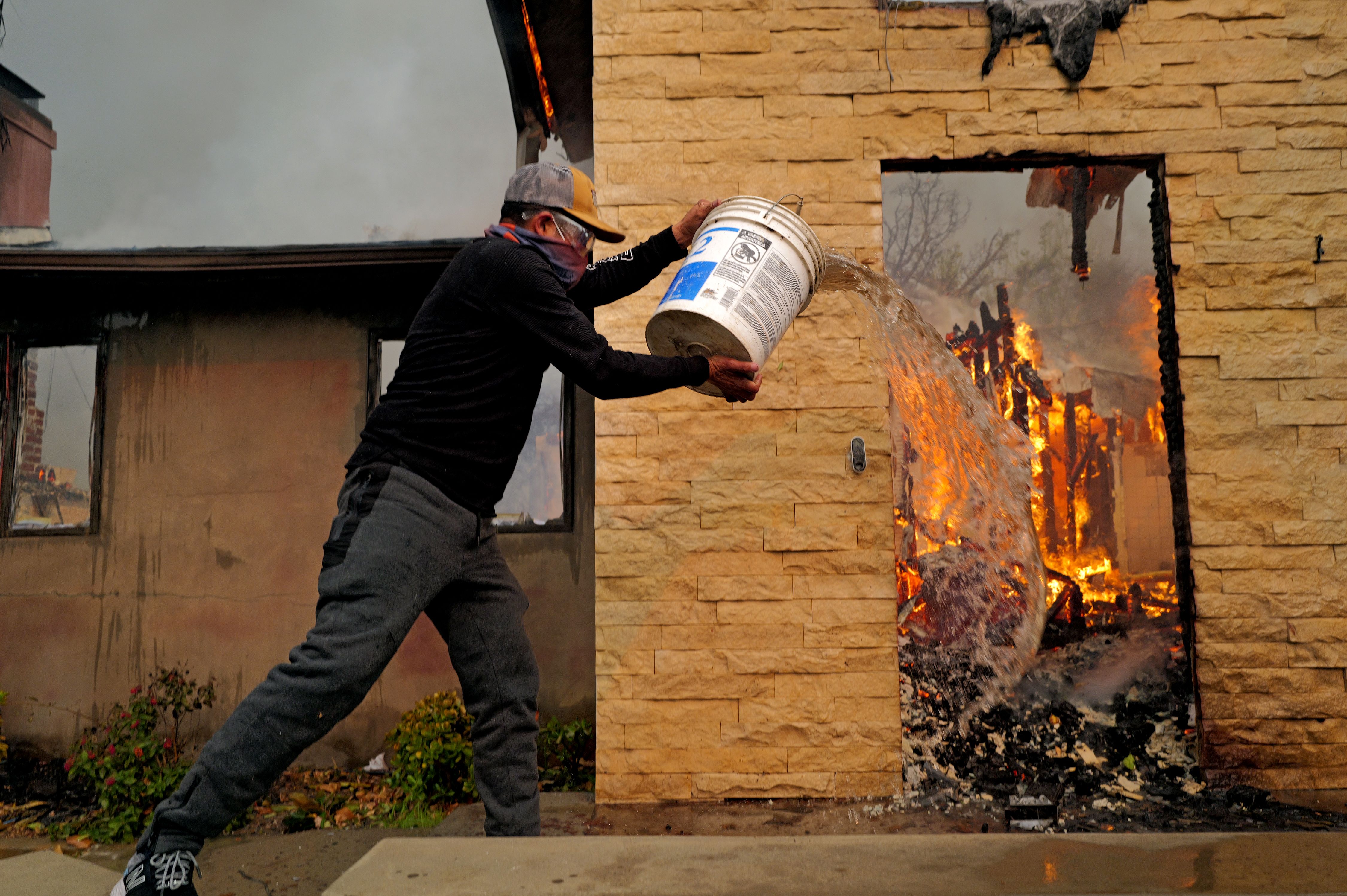 A man pours water on a house destroyed from the Eaton Fire in the Altadena neighborhood on January 08, 2025 in PASADENA, CALIFORNIA. 