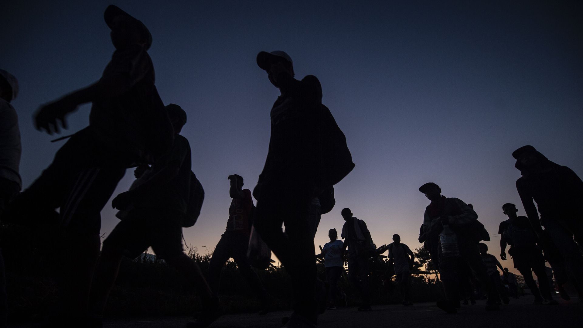 Silhouettes of people marching in a caravan before a pink and blue dark sky.