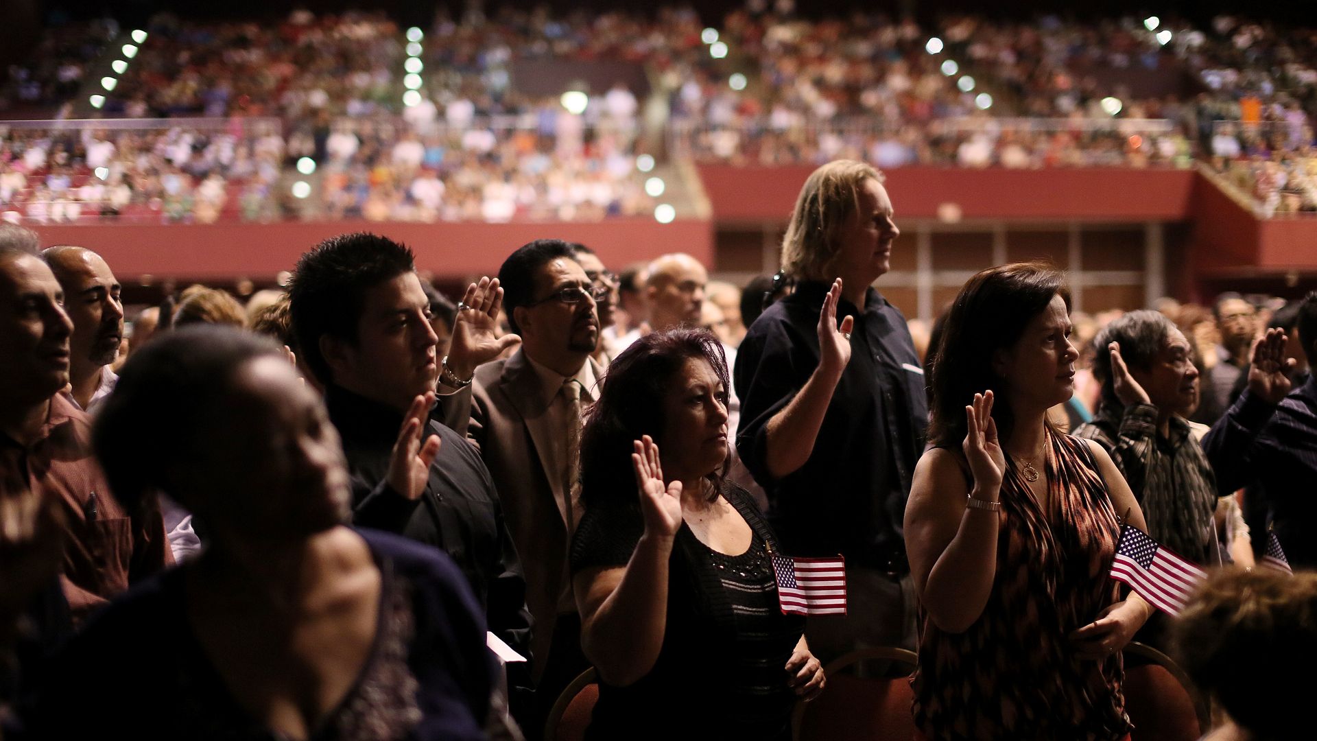 Citizens from around the world hold up their right hands as they recite the Pledge of Allegiance during a Naturalization Ceremony