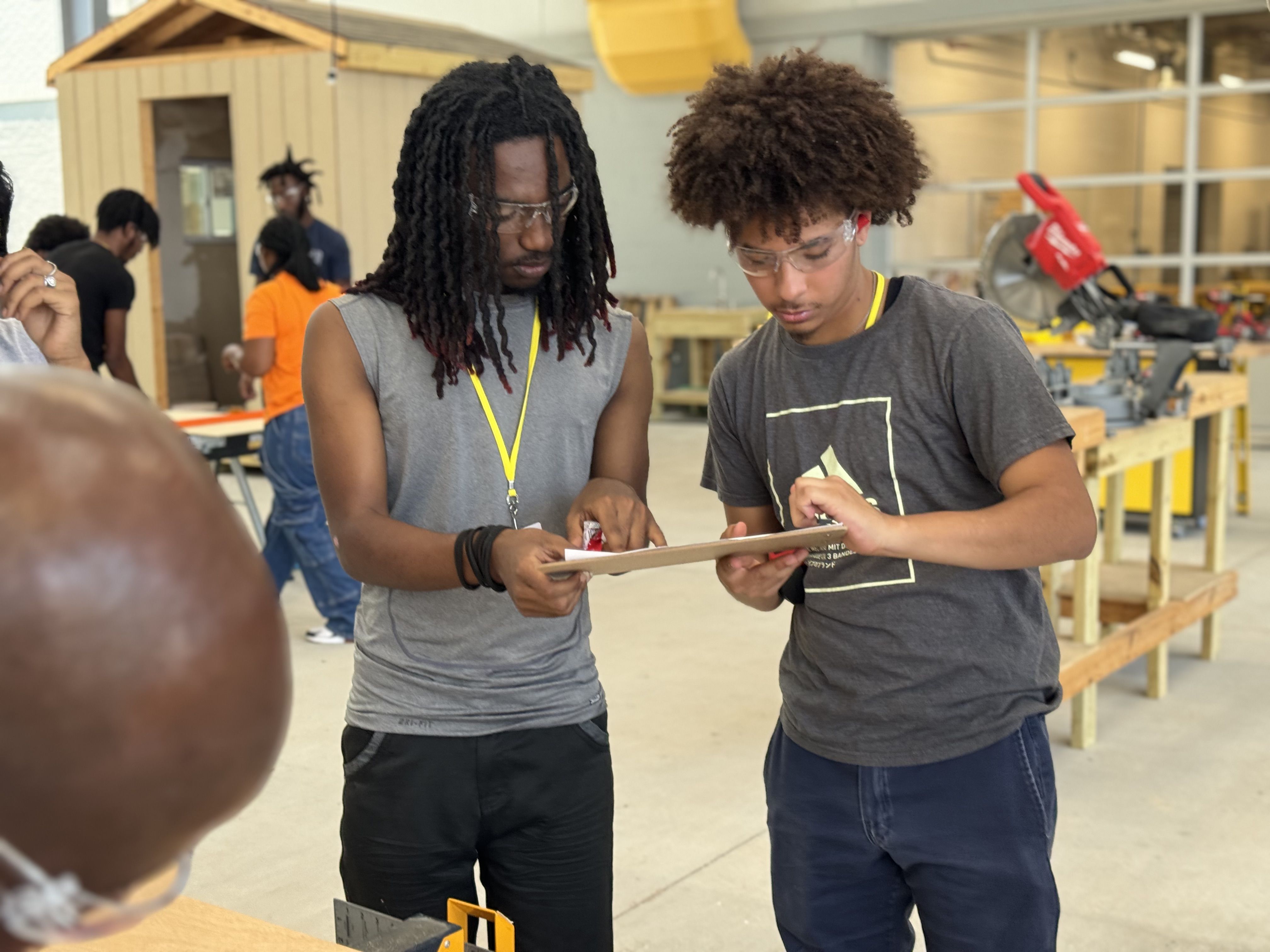 Two young men lean together, looking over a clipboard.