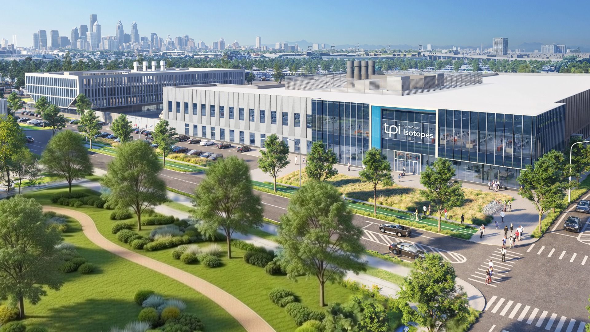 Modern office campus with a glass-front building and blue entry frame, green lawns and trees, a parking lot and a distant city skyline beneath a clear blue sky.