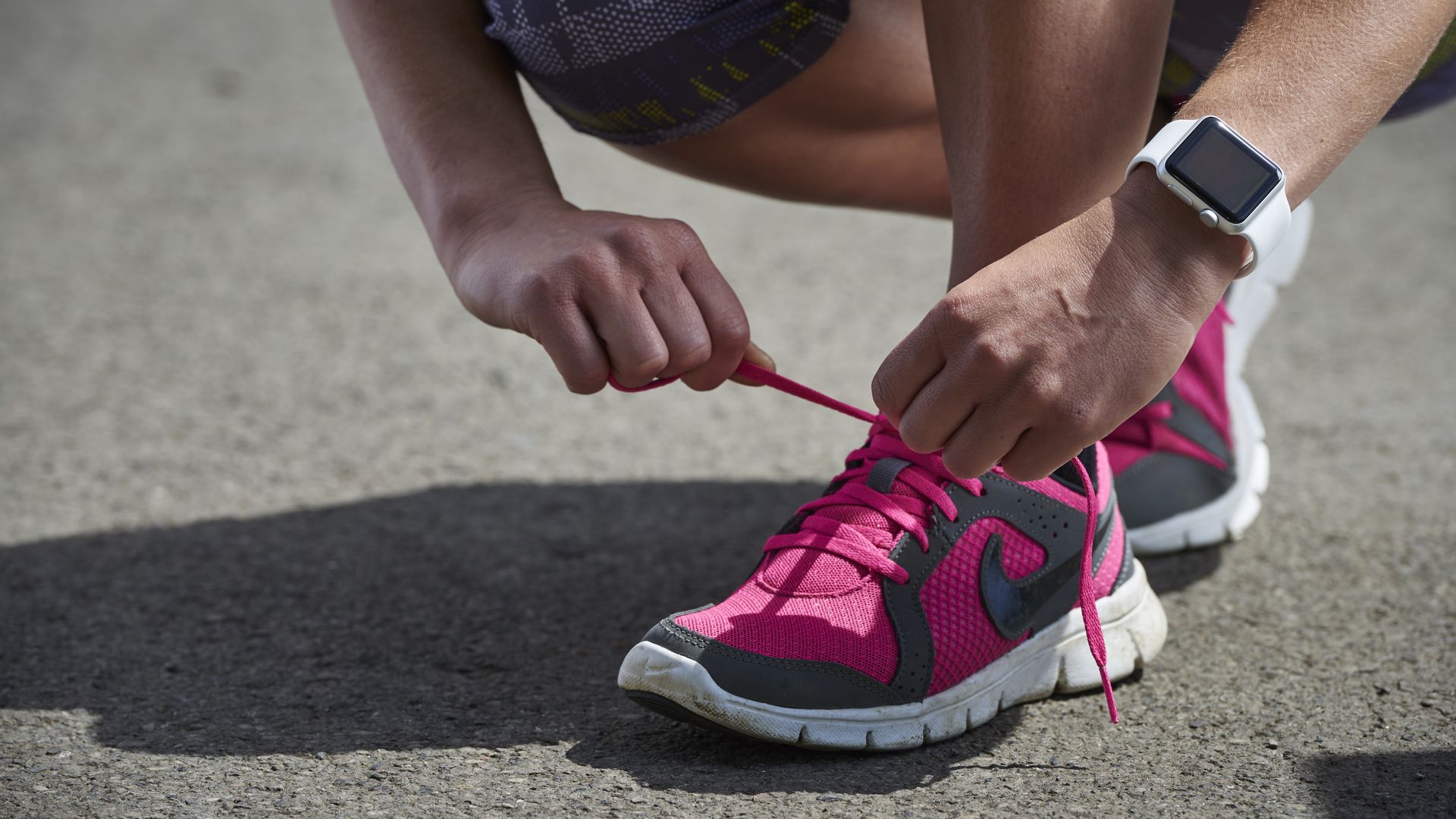 woman tying a sneaker while wearing a smartwatch