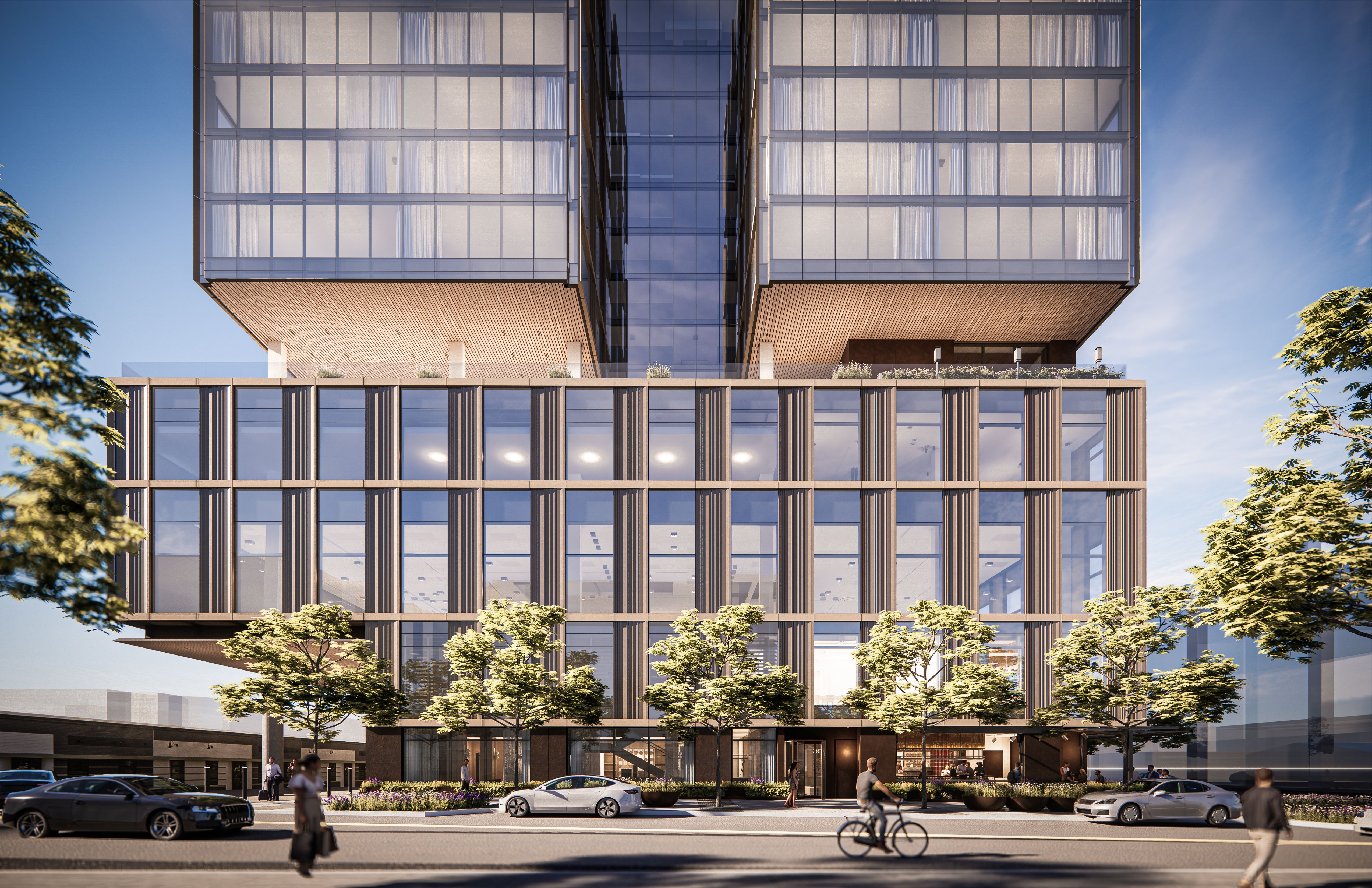 Modern glass office building with a central glass bridge and grid-like windows; wood-toned base, greenery on balconies, busy street with cars, cyclists, and pedestrians against a blue sky.