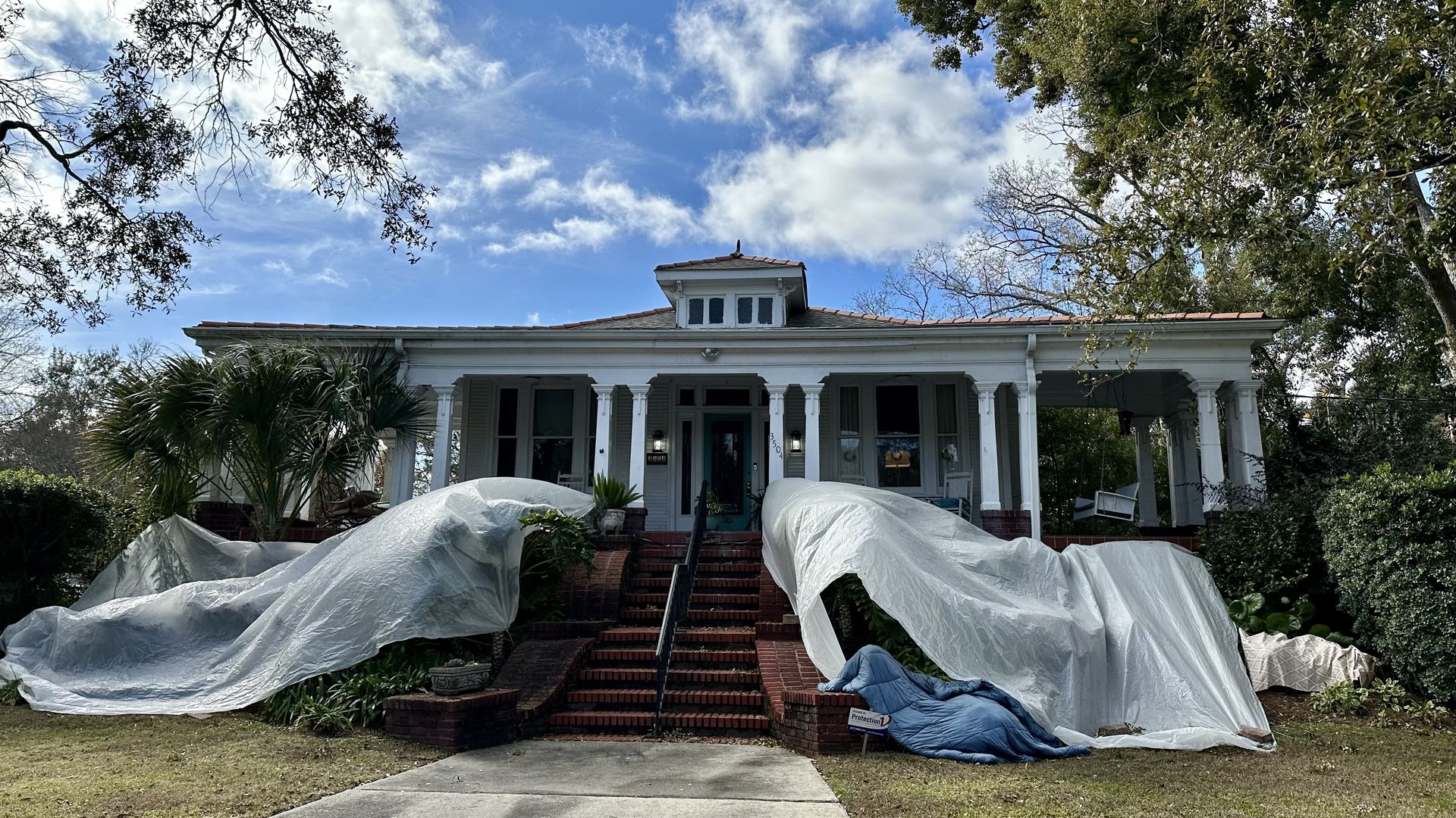 Photo shows tarps covering plants in front of a large home in New Orleans.