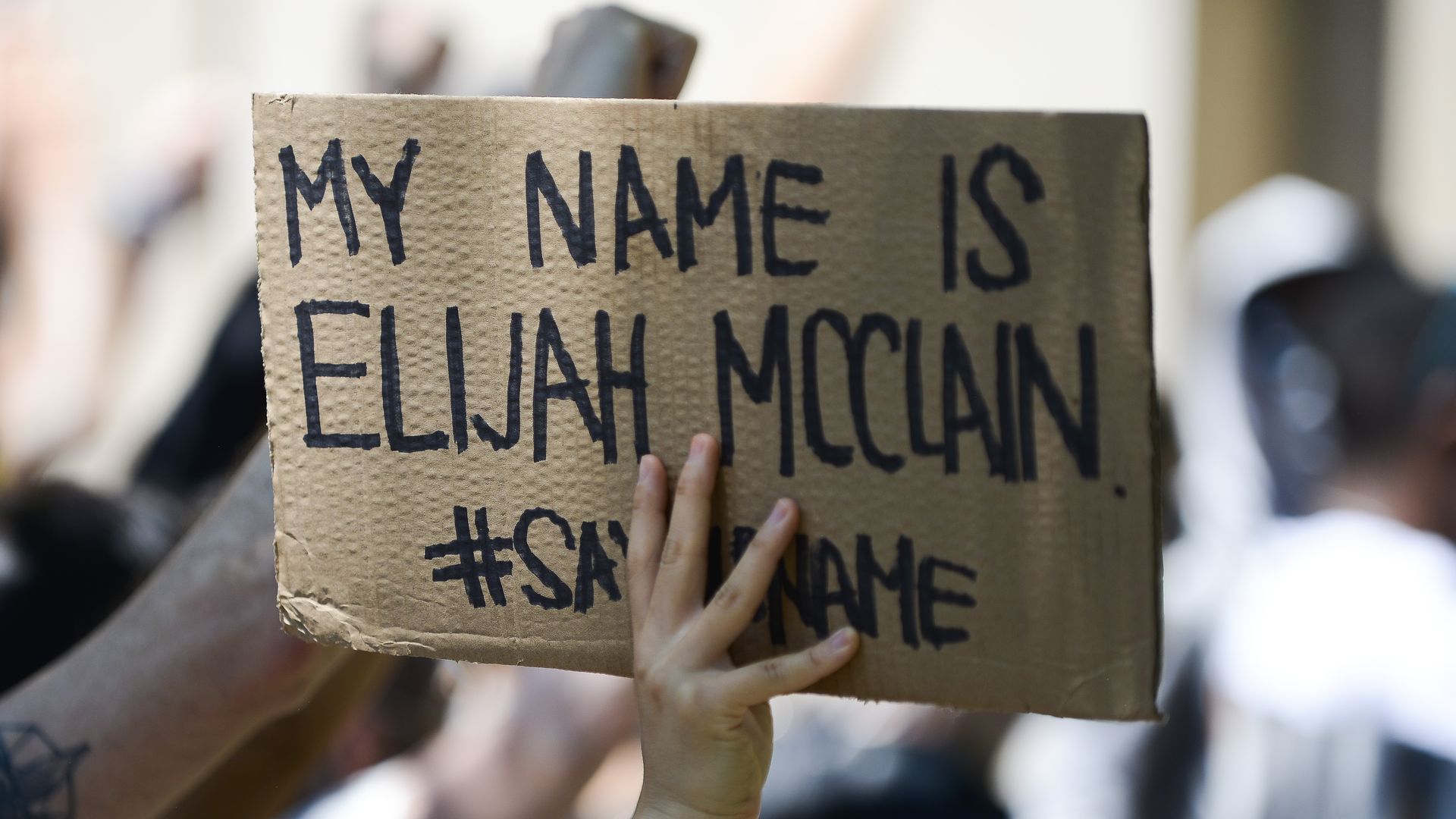 Picture of a hand holding a cardboard that says "my name is Elijah McClain"
