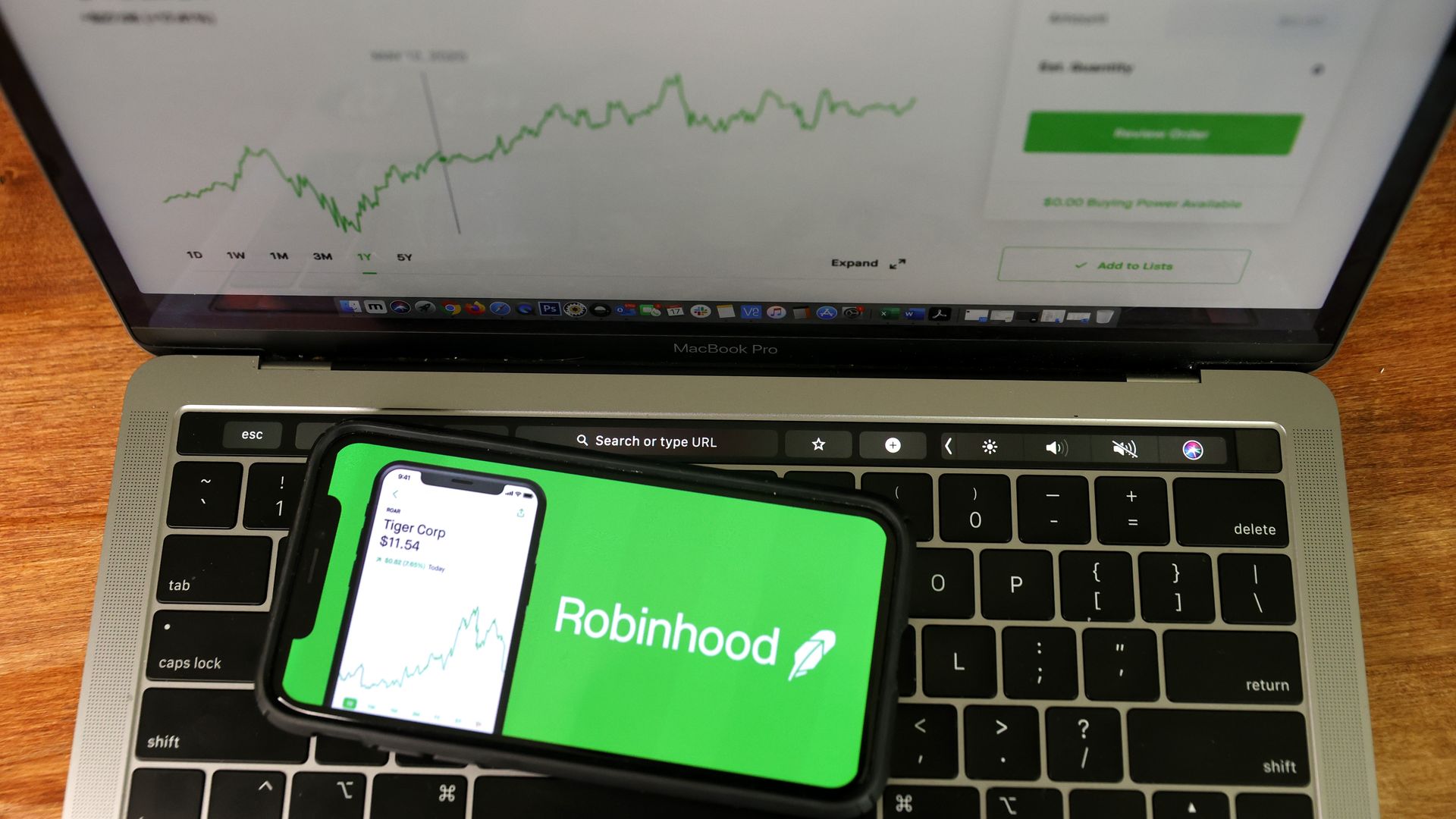 A smartphone displaying the RobinHood app is seen on the keyboard of a laptop.
