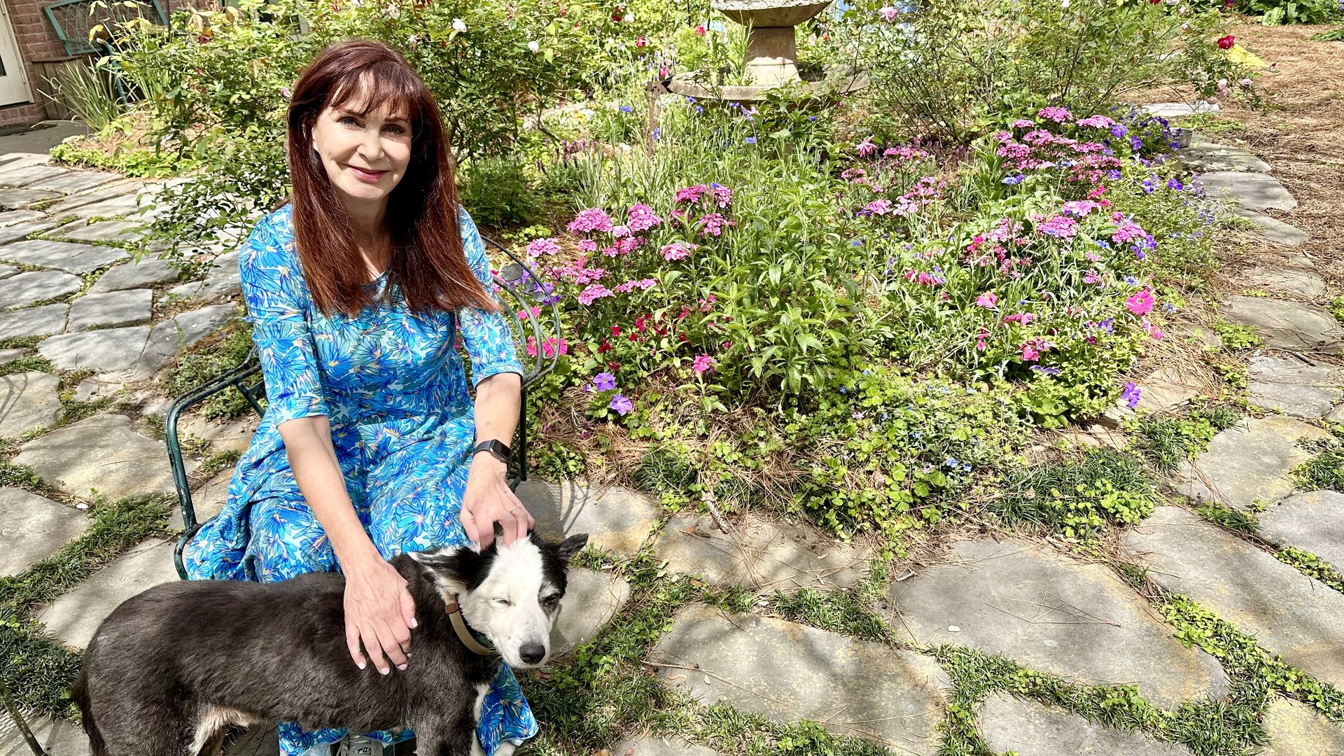 Photo shows WDSU chief meteorologist Margaret Orr with her dog Bleu sitting in front of her flower garden.