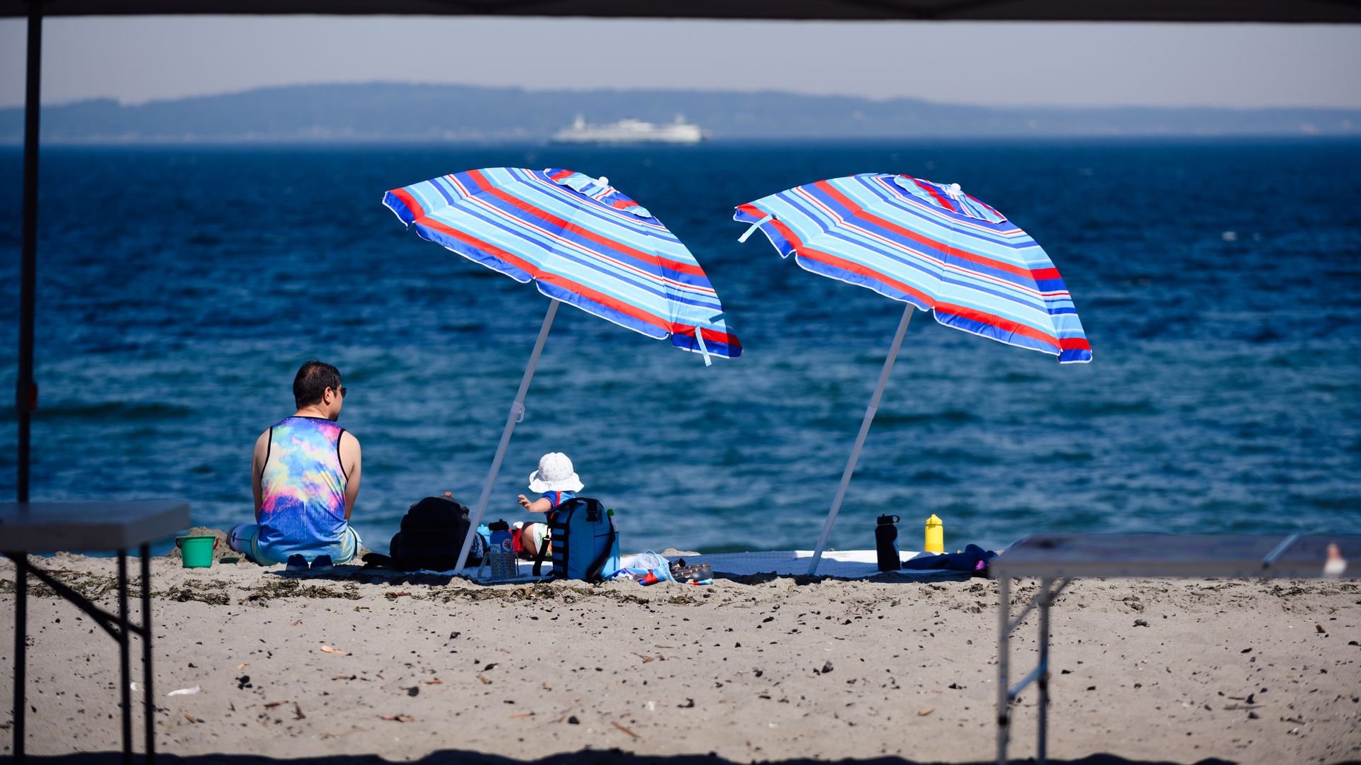 Bright umbrellas with people beneath on a Seattle beach during a heat wave. 