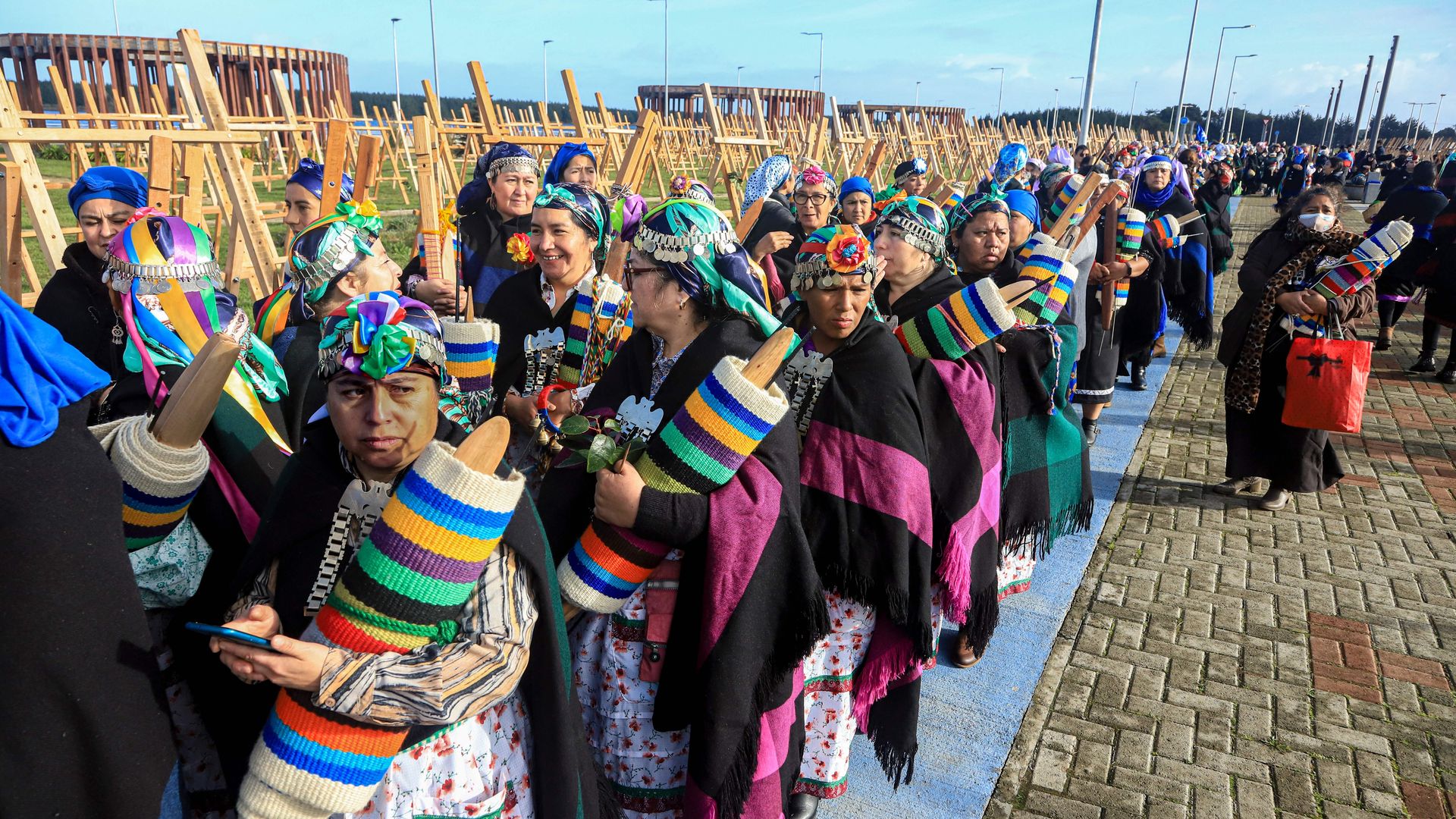 Chilean Mapuche weavers are lined up while holding rows of fabric to weave 