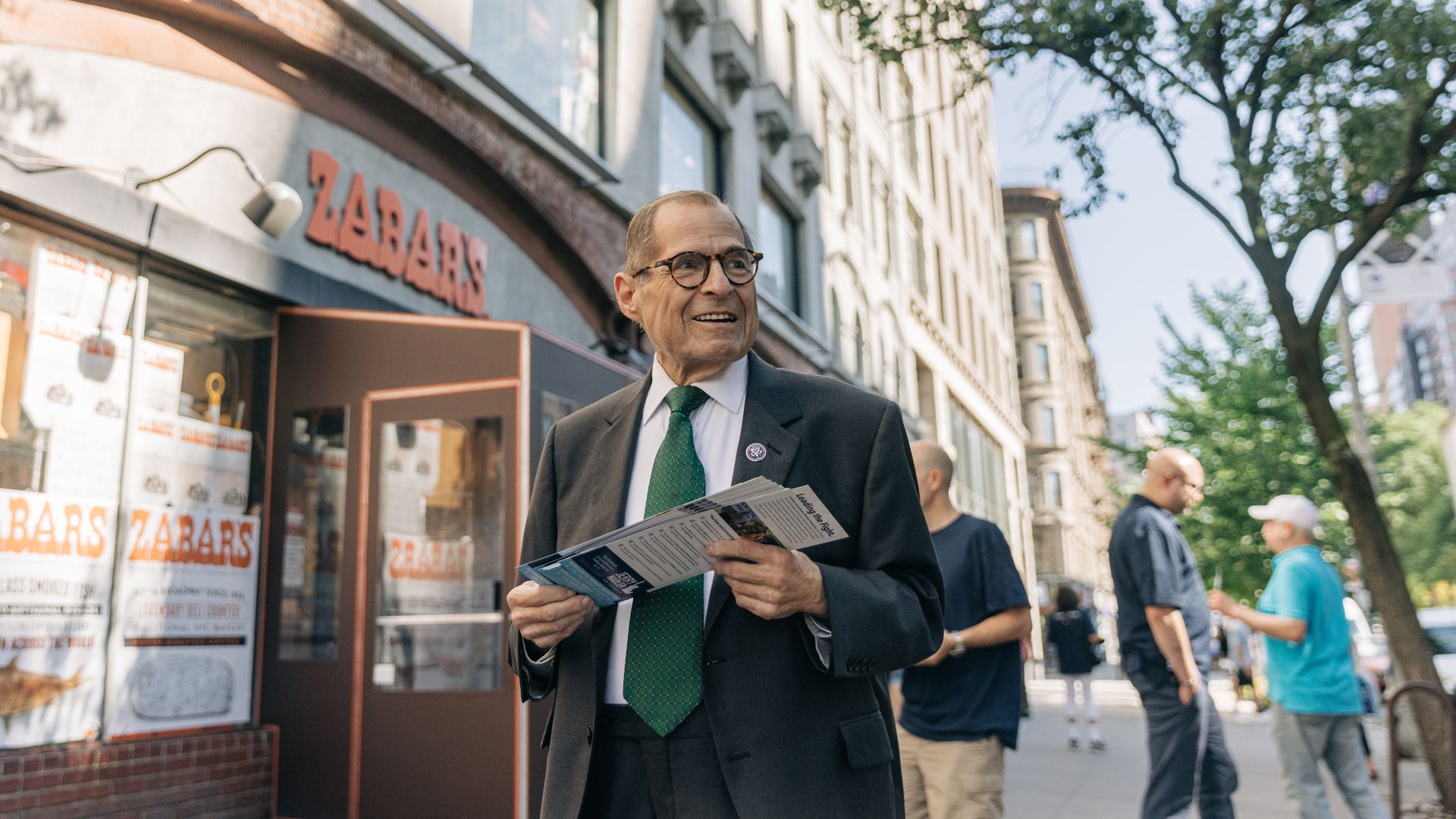 Rep. Jerry Nadler, in a gray suit, white shirt and green tie, holds campaign literature while campaigning in front of Zabar's.