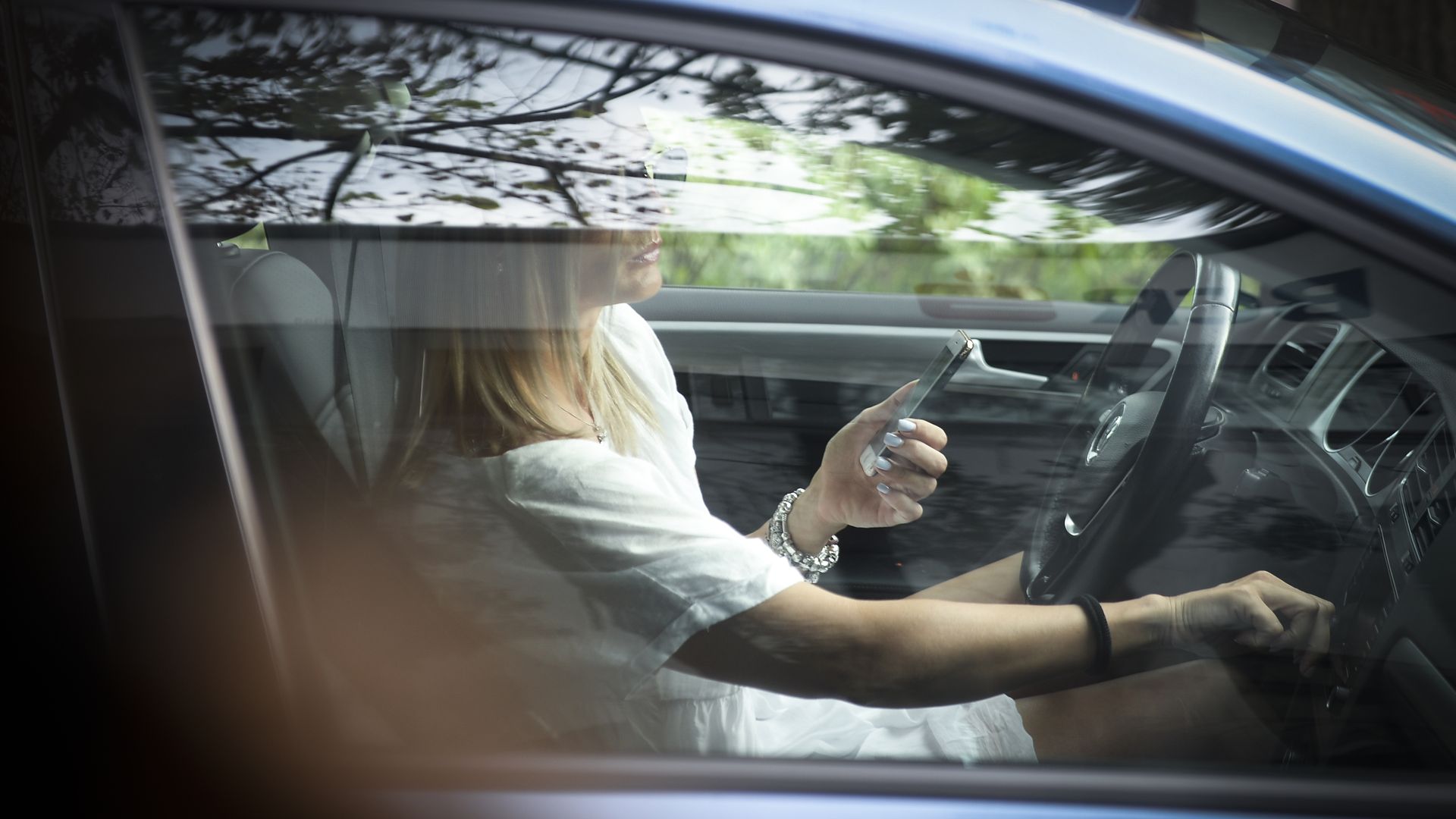 A woman in a car with a phone in one hand adjusts the radio with her other.