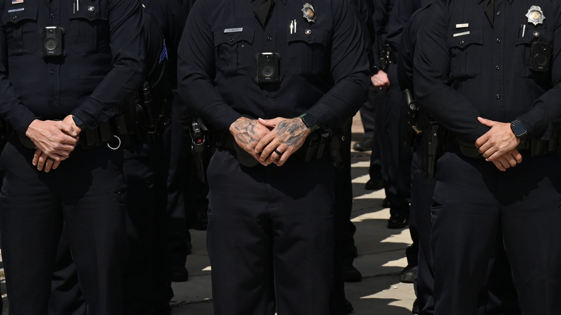 Uniformed Denver police officers stand with their hands held together in a photo that shows them from the shoulders down.