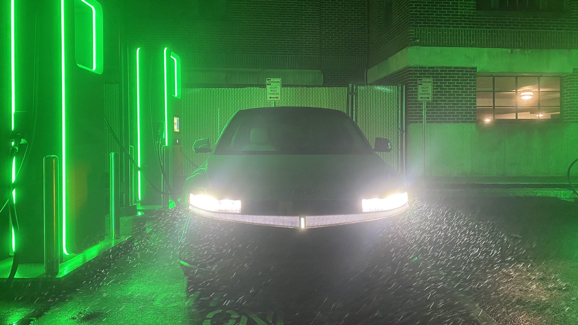 A Hyundai Ioniq 5, plugged into a green-lit Electrify America charging station at night.