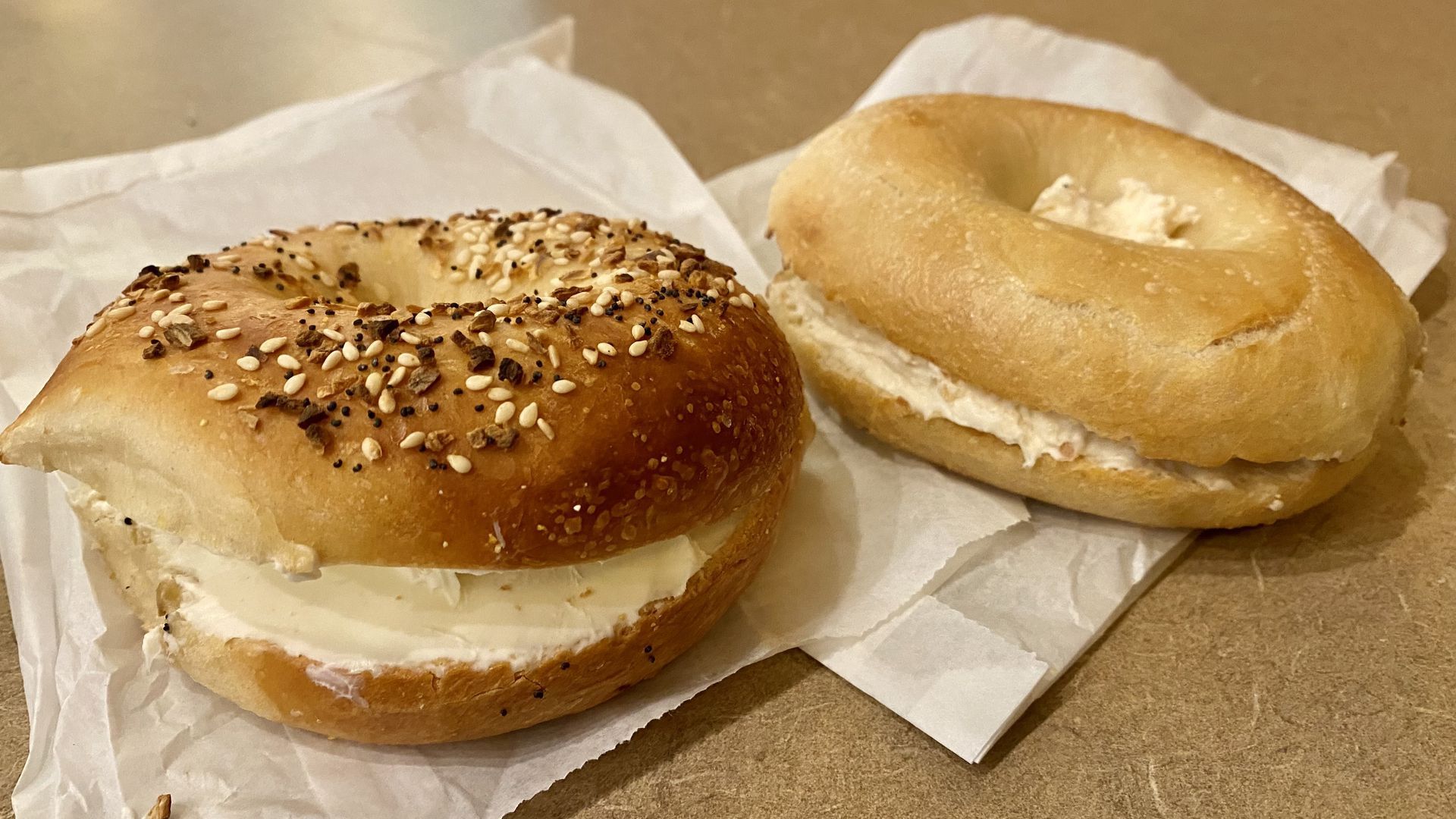 Everything bagel with cream cheese next to a plain bagel. 