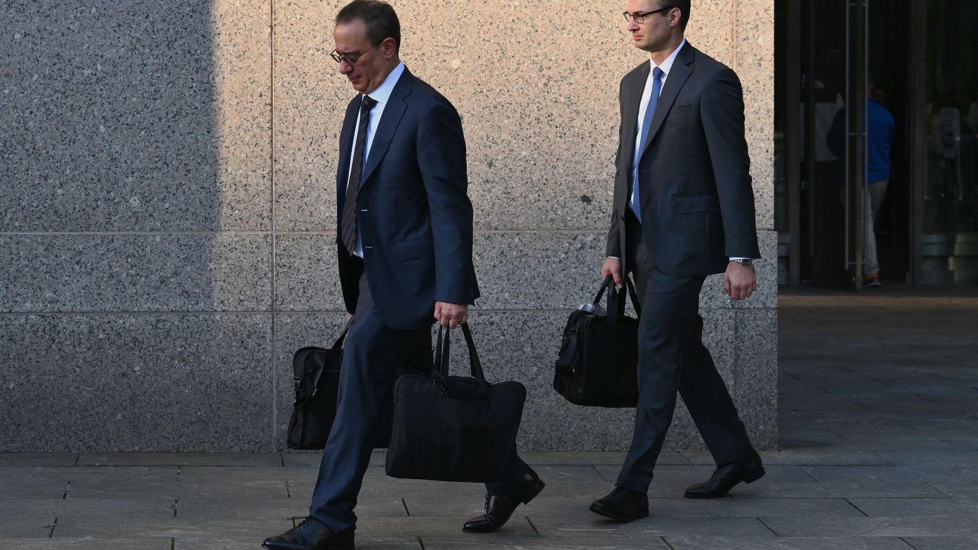 Men in business suits, carrying briefcases, walk to the left, in profile, with the sun low in the sky.