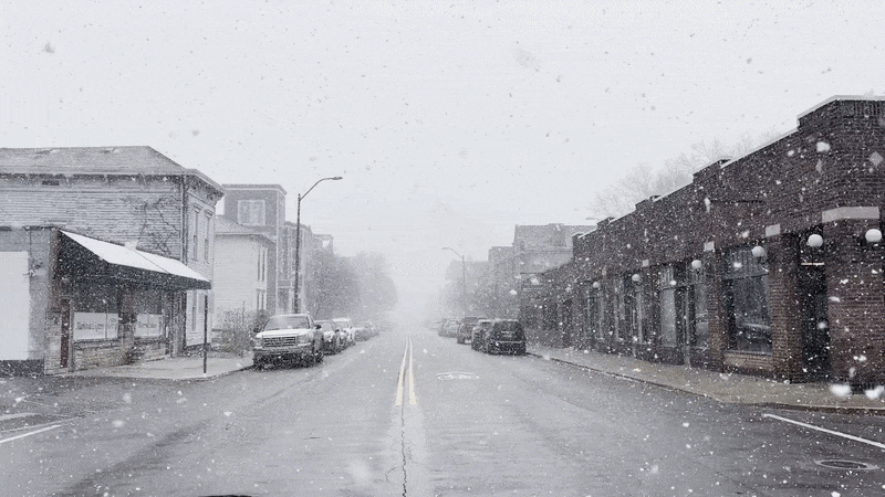 A gif of snow falling on a city street.