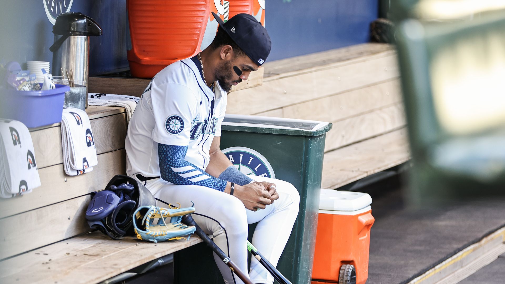 A baseball player sits with his head bowed in the dugout before a game. 