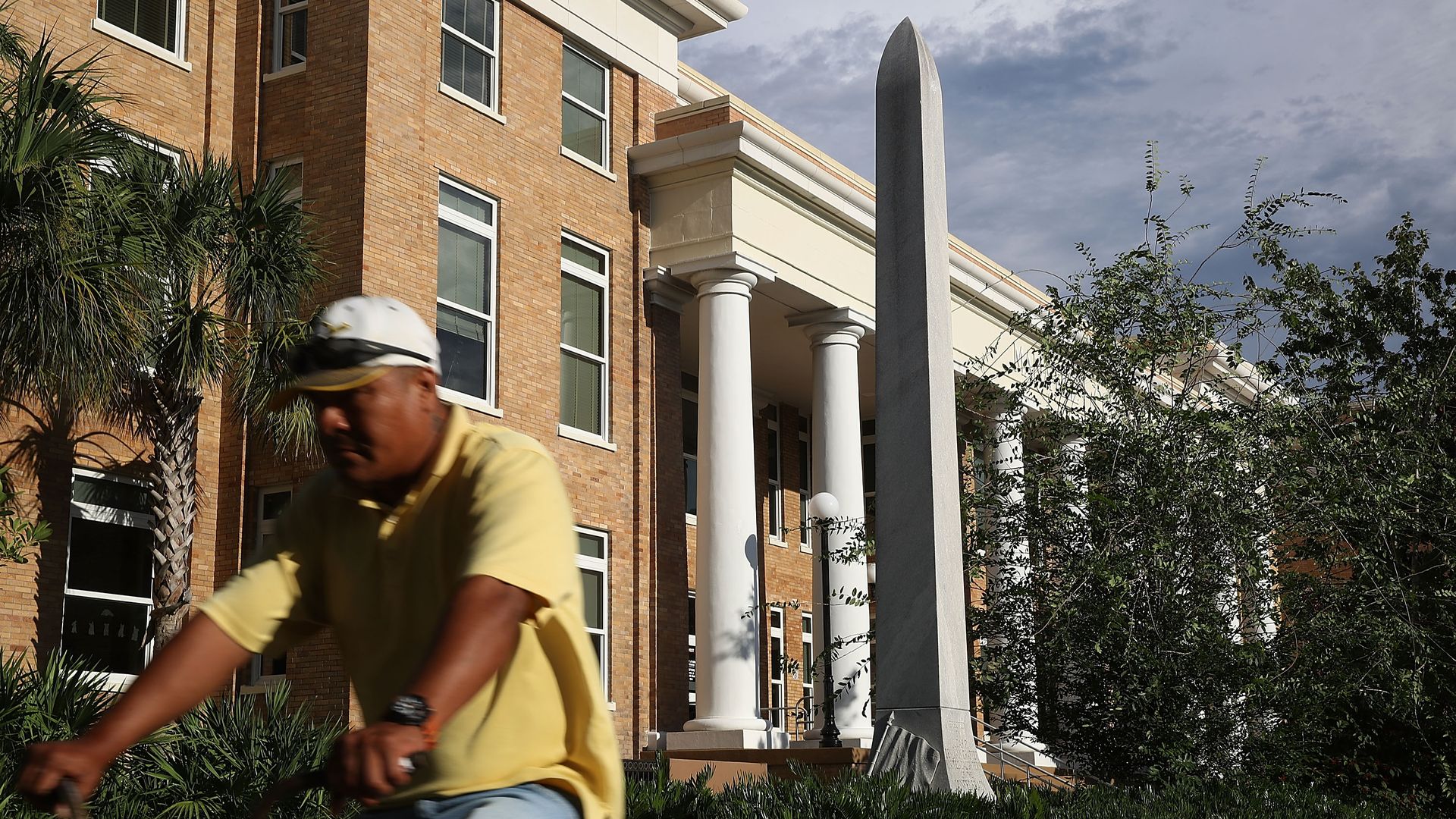 A man rides a bike past a tall confederate monument
