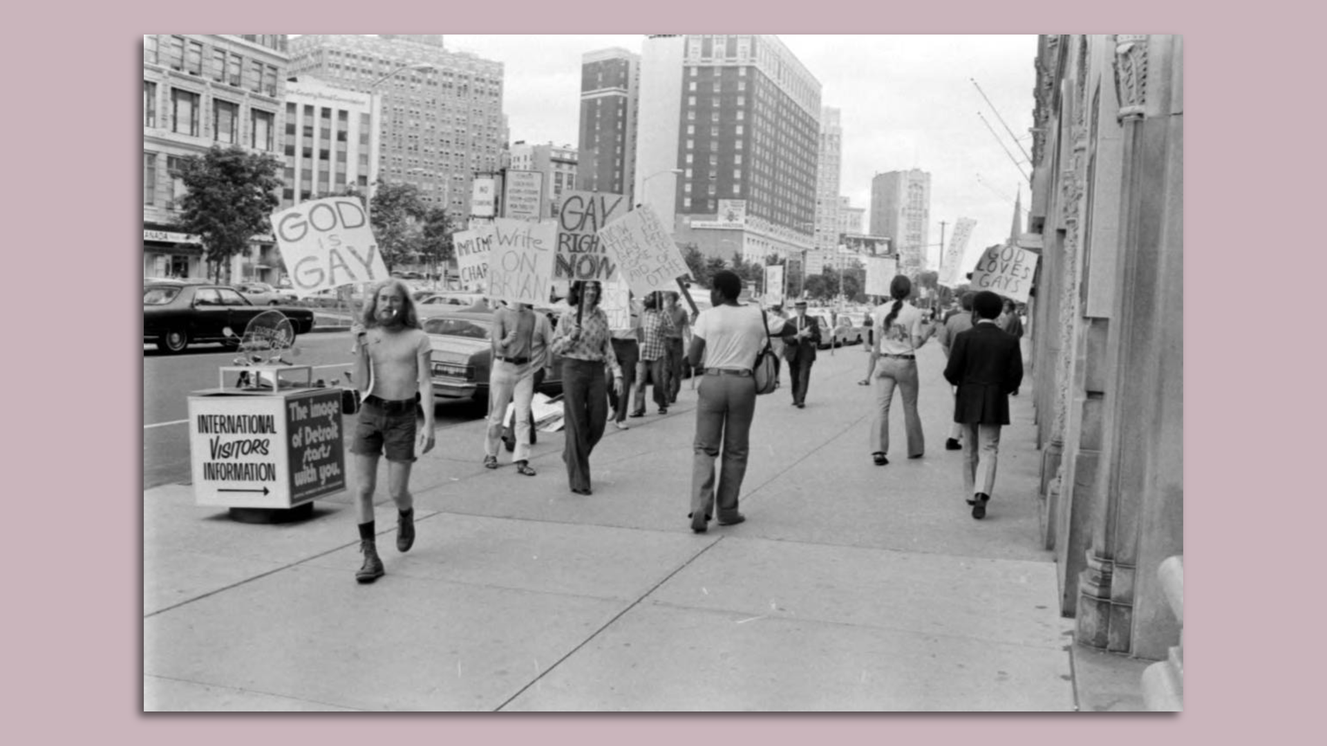 Protesters in a historical black and white photograph hold signs including "God Loves Gays" and "Write On Brian".