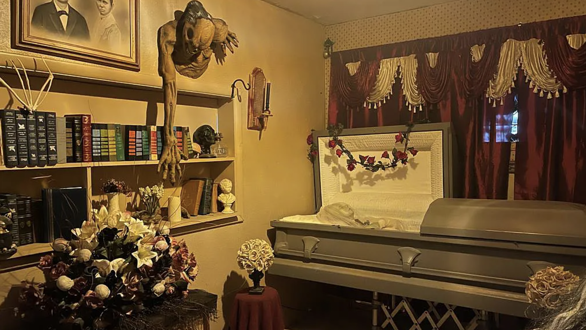 A bedroom with a coffin and flowers and scary red drapes