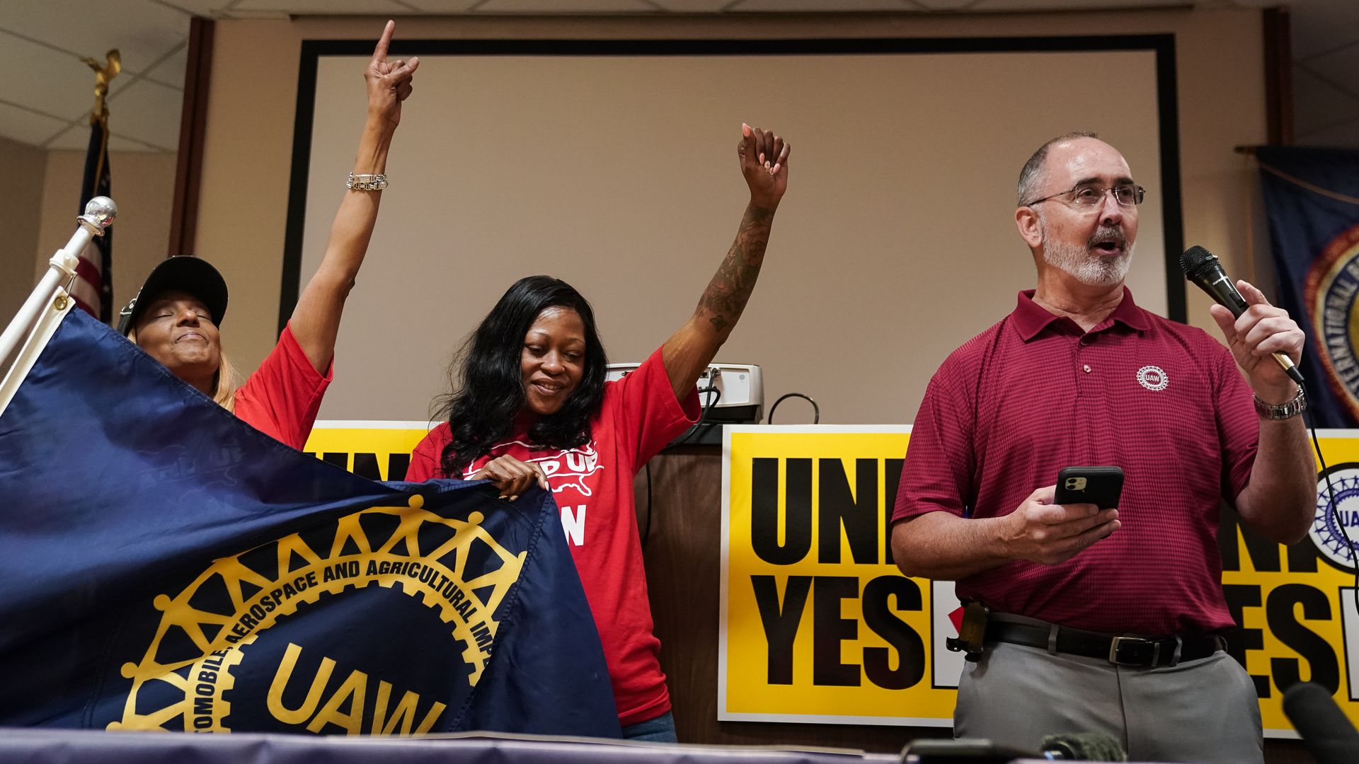 United Auto Workers (UAW) President Shawn Fain, right, wearing a red union polo shirt, holds a microphone while local organizers carrying a UAW banner raise their fists at a UAW vote watch party in Chattanooga, Tennessee