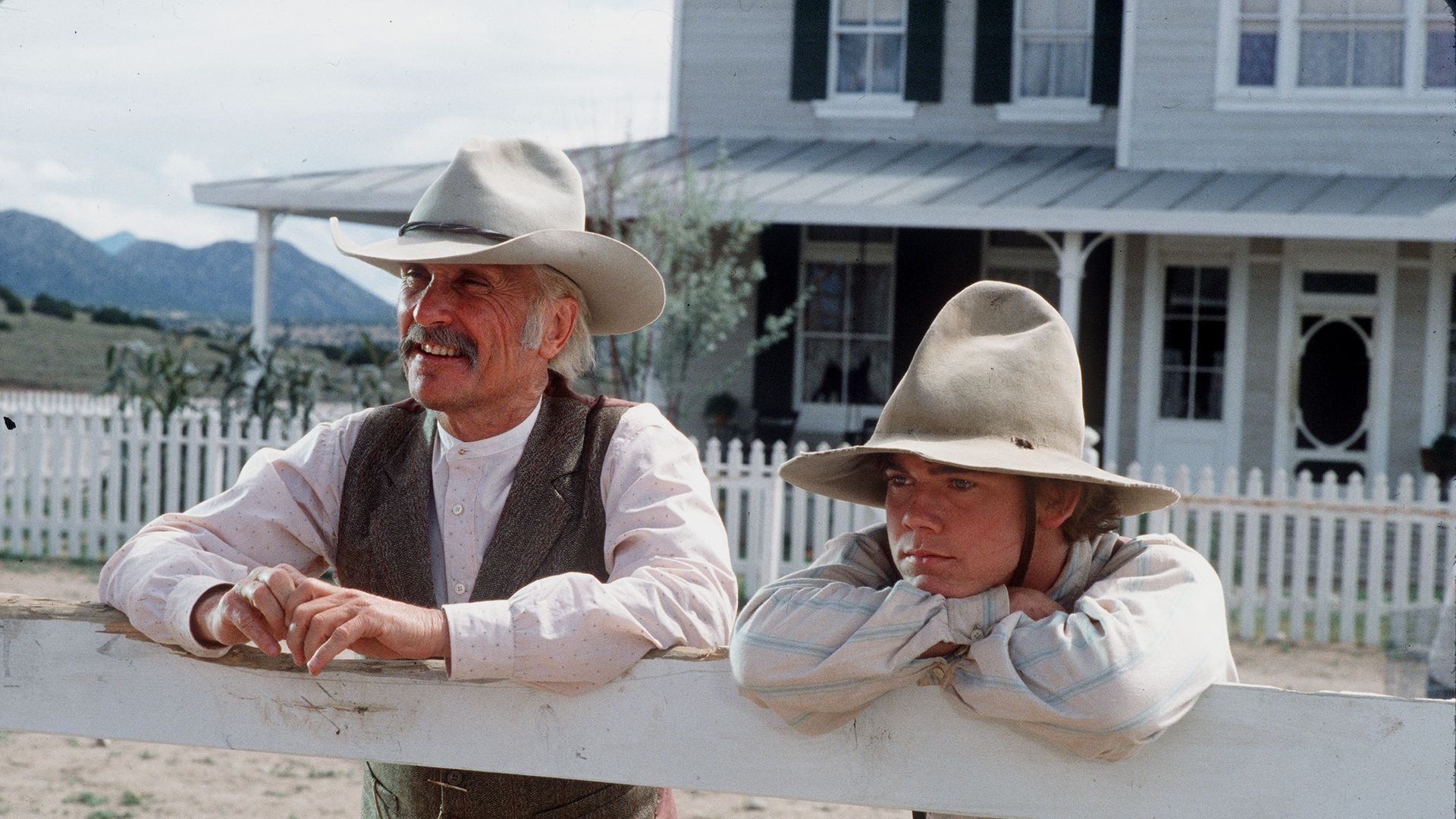 American actors Robert Duvall (as Augustus 'Gus' McCrae) and Rick Schroder (as Newt Dobbs) lean on a fence in a scene from the television miniseries 'Lonesome Dove,' 