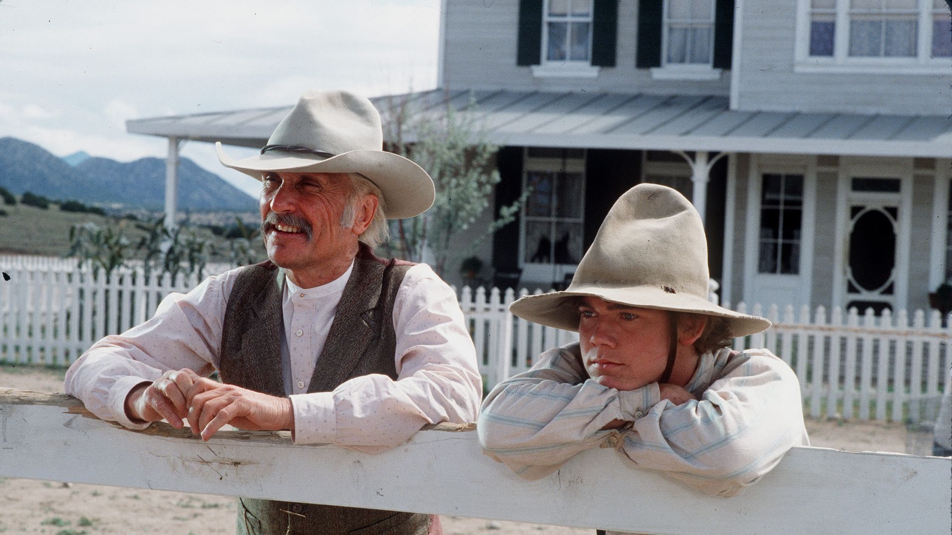 American actors Robert Duvall (as Augustus 'Gus' McCrae) and Rick Schroder (as Newt Dobbs) lean on a fence in a scene from the television miniseries 'Lonesome Dove,'