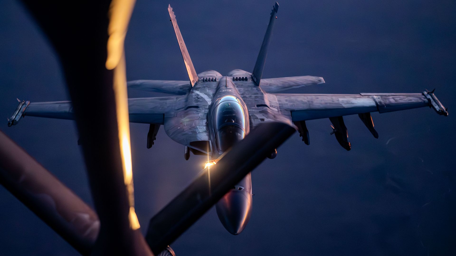 An F/A-18 lines up with a KC-135 for midair refueling. The photo is tinted a bit blue.