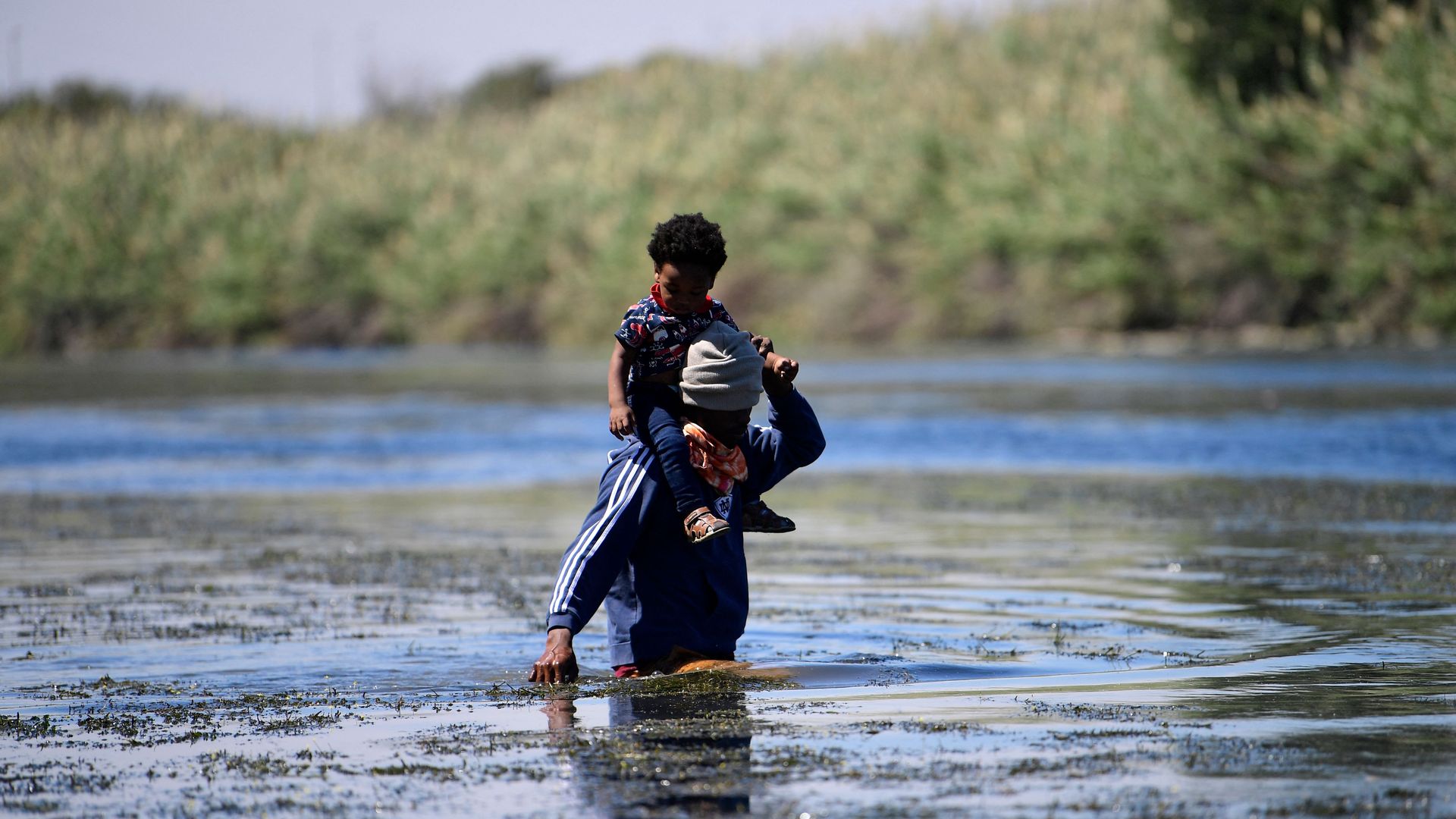 A Haitian migrant with a child on their shoulders is seen crossing the U.S.-Mexico border at the Rio Grande River.