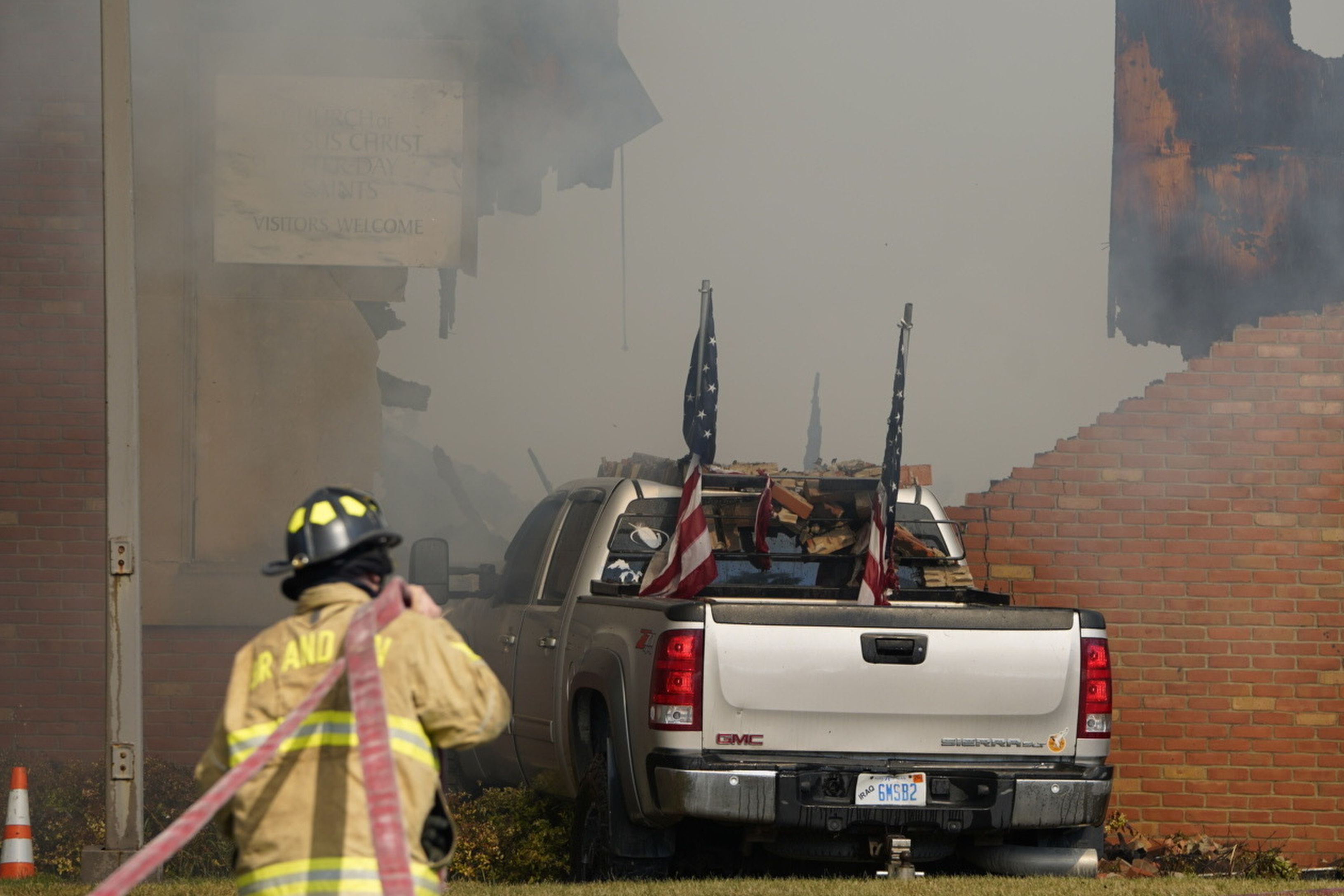 A vehicle that was rammed into the building is surrounded by smoke as a firefighter works on the scene at the Church of Jesus Christ of Latter-day Saints in Grand Blanc, Mich., Sunday, Sept. 28, 2025. (Lukas Katilius/The Flint Journal via AP)