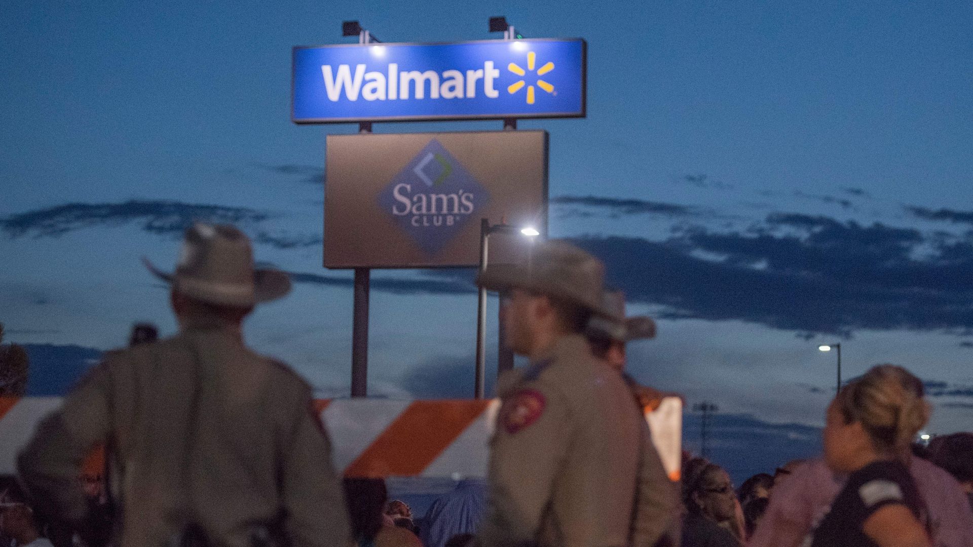 In this image, law enforcement stand in a Walmart parking lot at night. The Walmart logo is on a tall sign behind them.