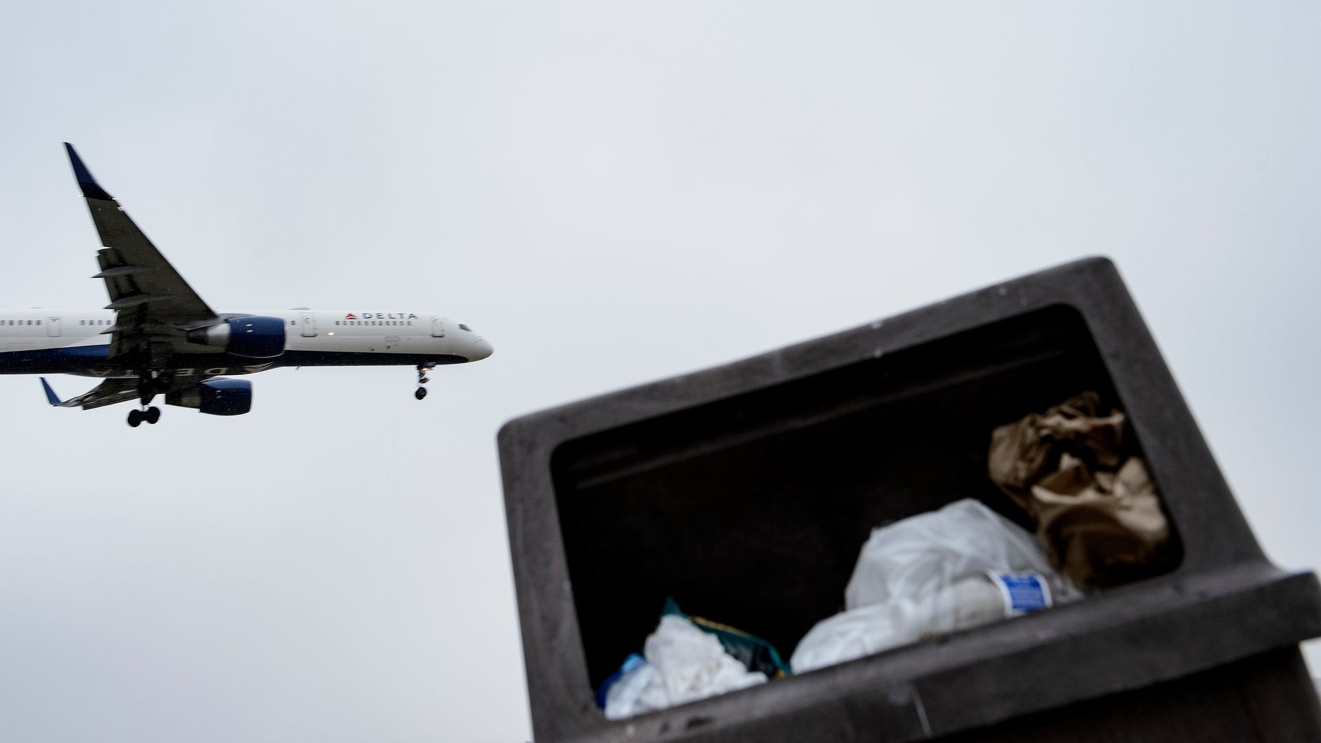 In this image, a plain flies overhead of a trash can.