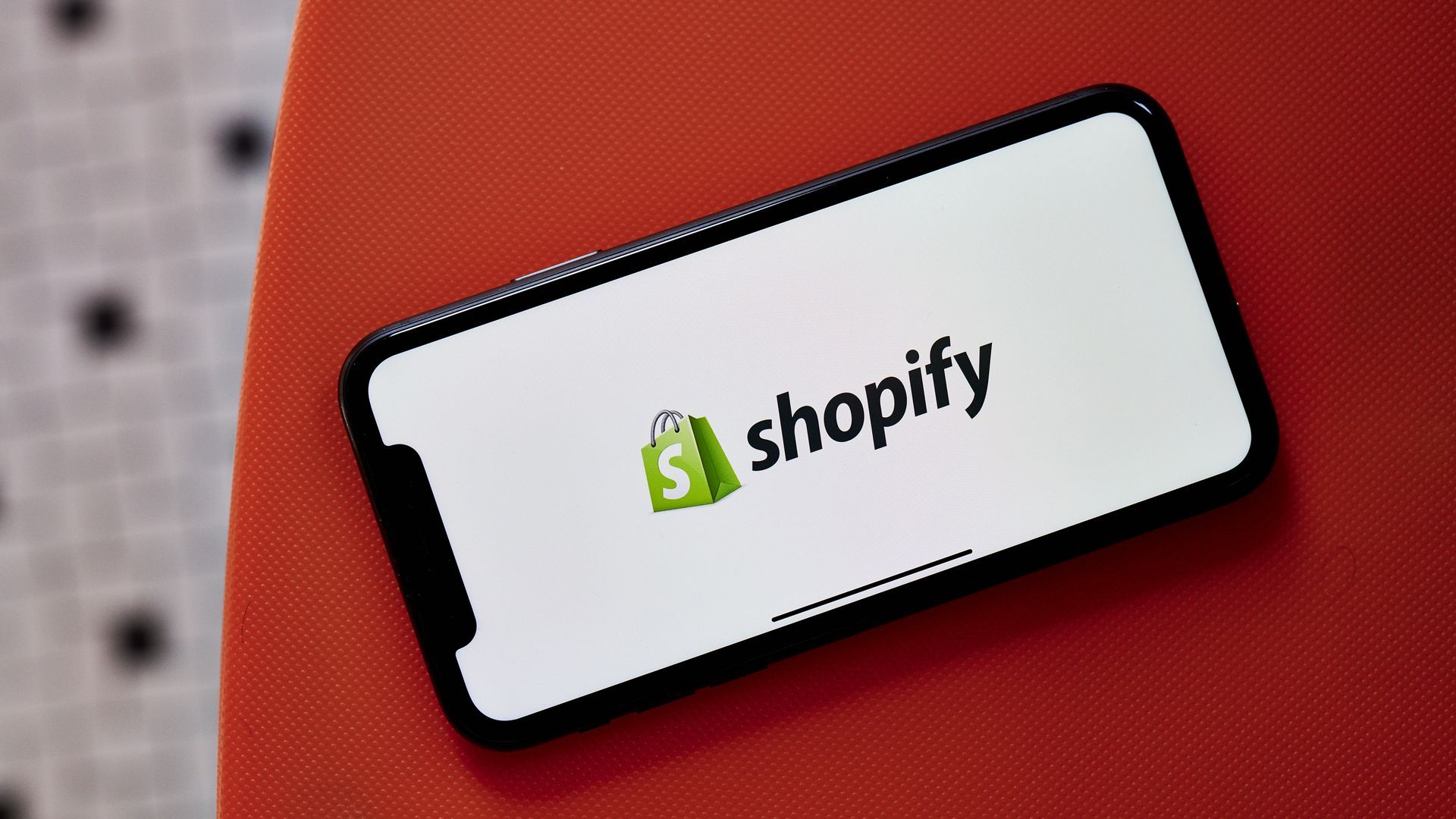 The Shopify logo, a green shopping bag with the letter S spelled in white, appears on a white background on a touchscreen mobile phone.