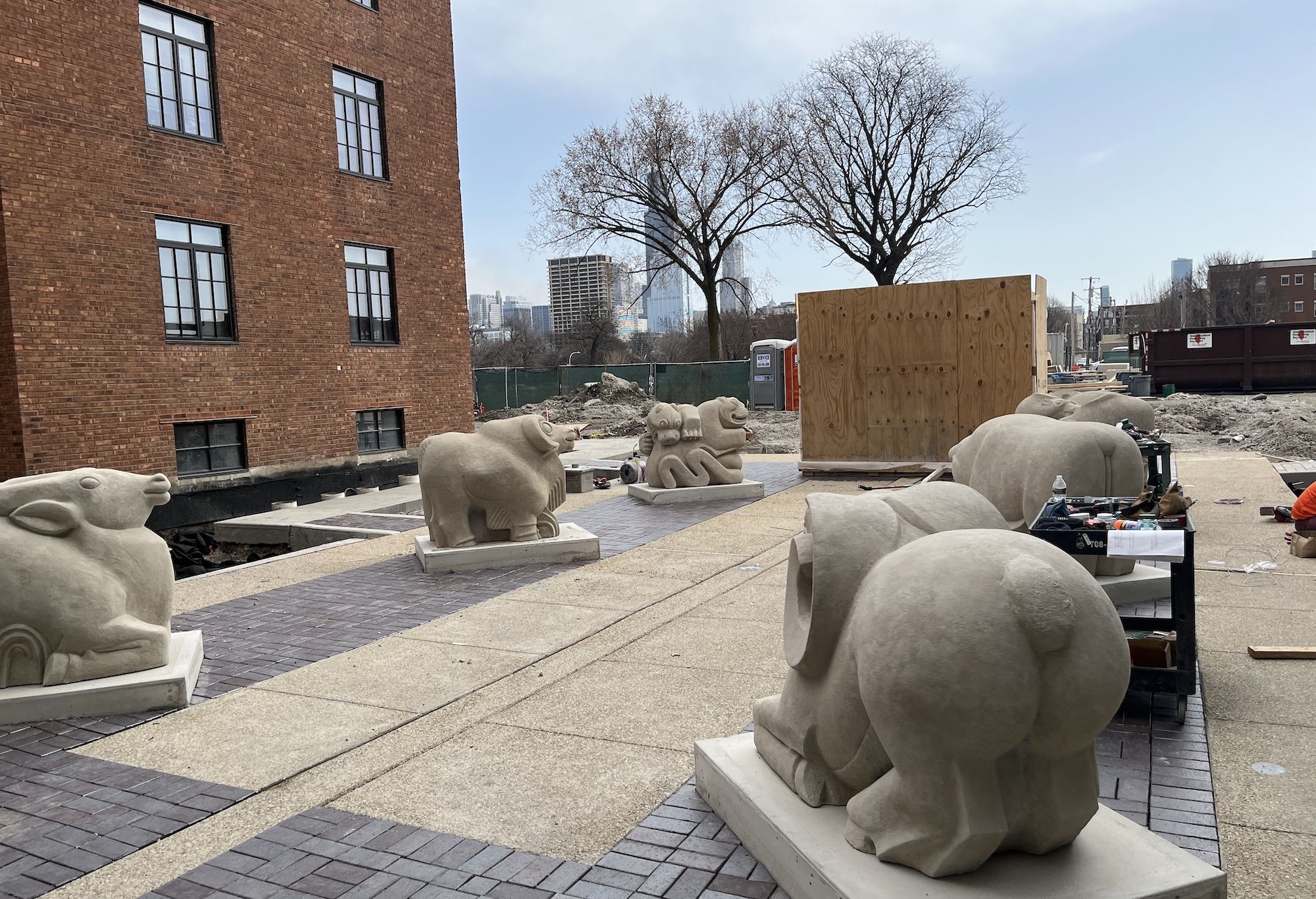 A courtyard of concrete sculptures of animals with a brick building and the Sears Tower in the distance.