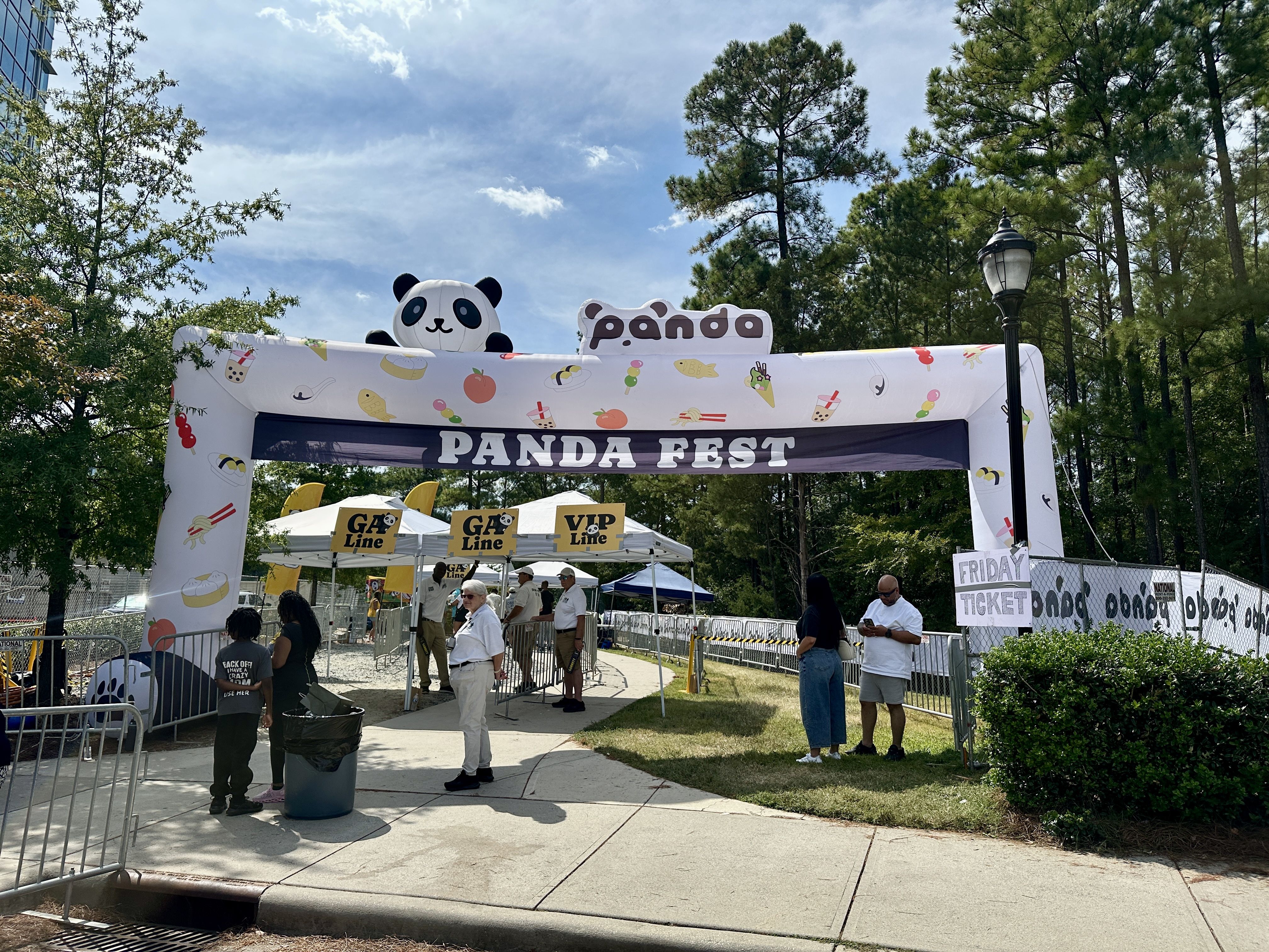 Outdoor entrance to Panda Fest with white inflatable arch decorated with food icons and a large panda figure on top, ticket booths labeled "GA Line" and "VIP Line," and people waiting.