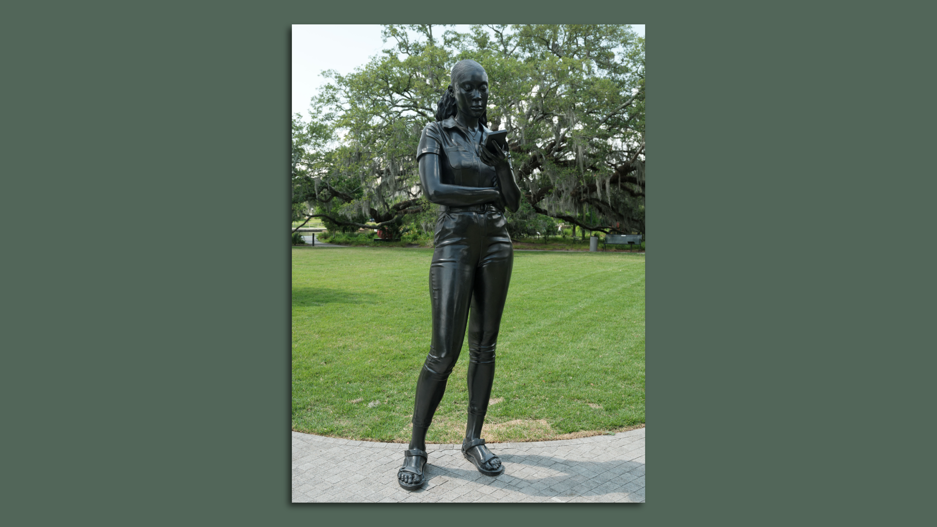 A photo of a bronze statue featuring the image of a woman as she looks at her phone.