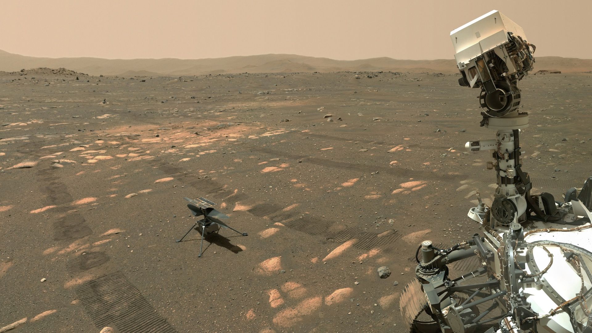 The little helicopter Ingenuity sits on Mars as the Perseverance rover looks at it, taking a photo