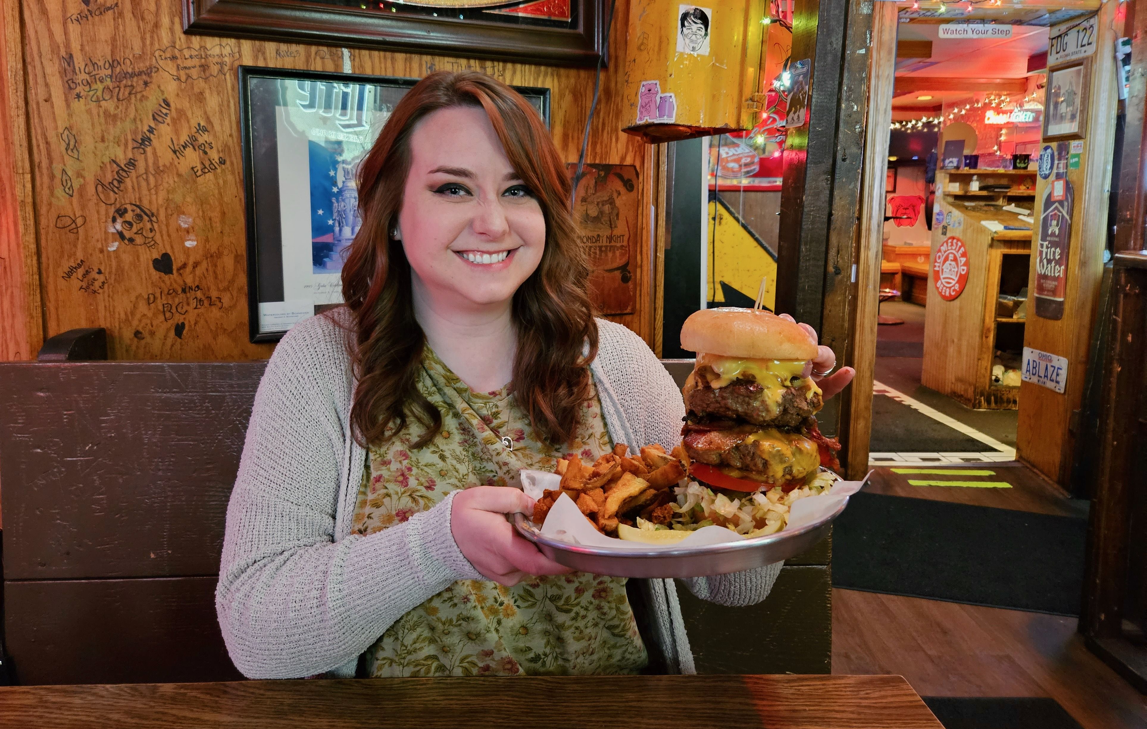Alissa holds a plate with a Thurmanator burger and fries.