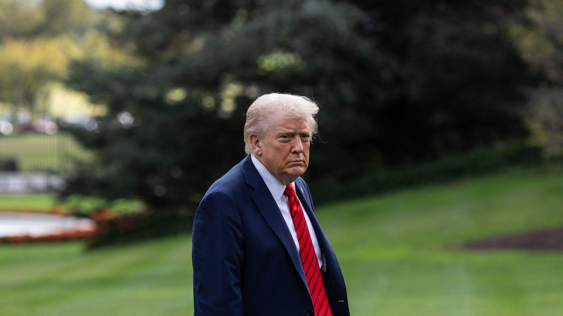 President Trump walks outside of the White House, wearing a red striped tie and blue suit jacket.