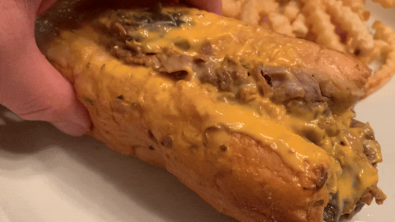 GIF of a man picking up a cheese and beef sandwich from a plate 