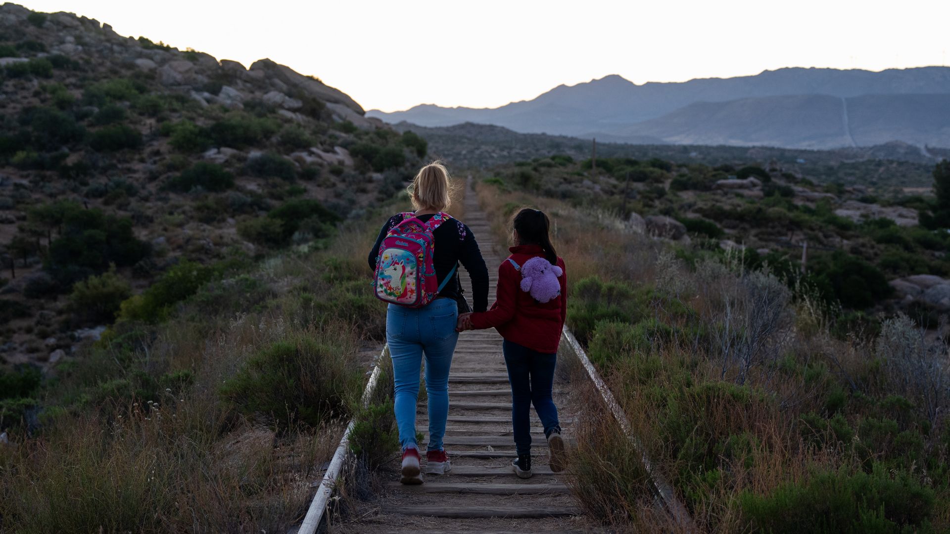 A woman and girl are seen from behind walking through railroads while crossing from Mexico into the U.S.