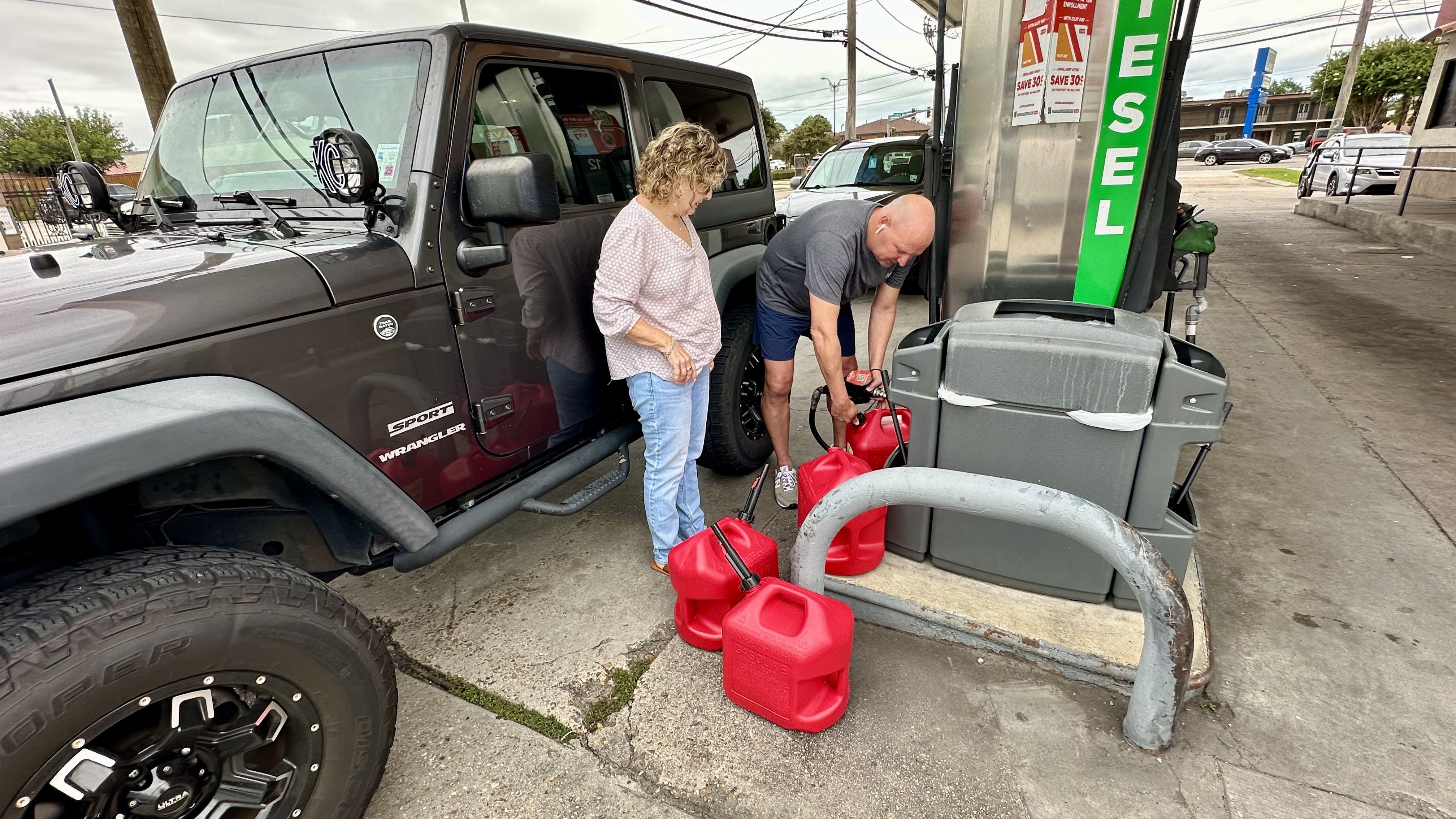 Photo shows people filling up red gas tanks.