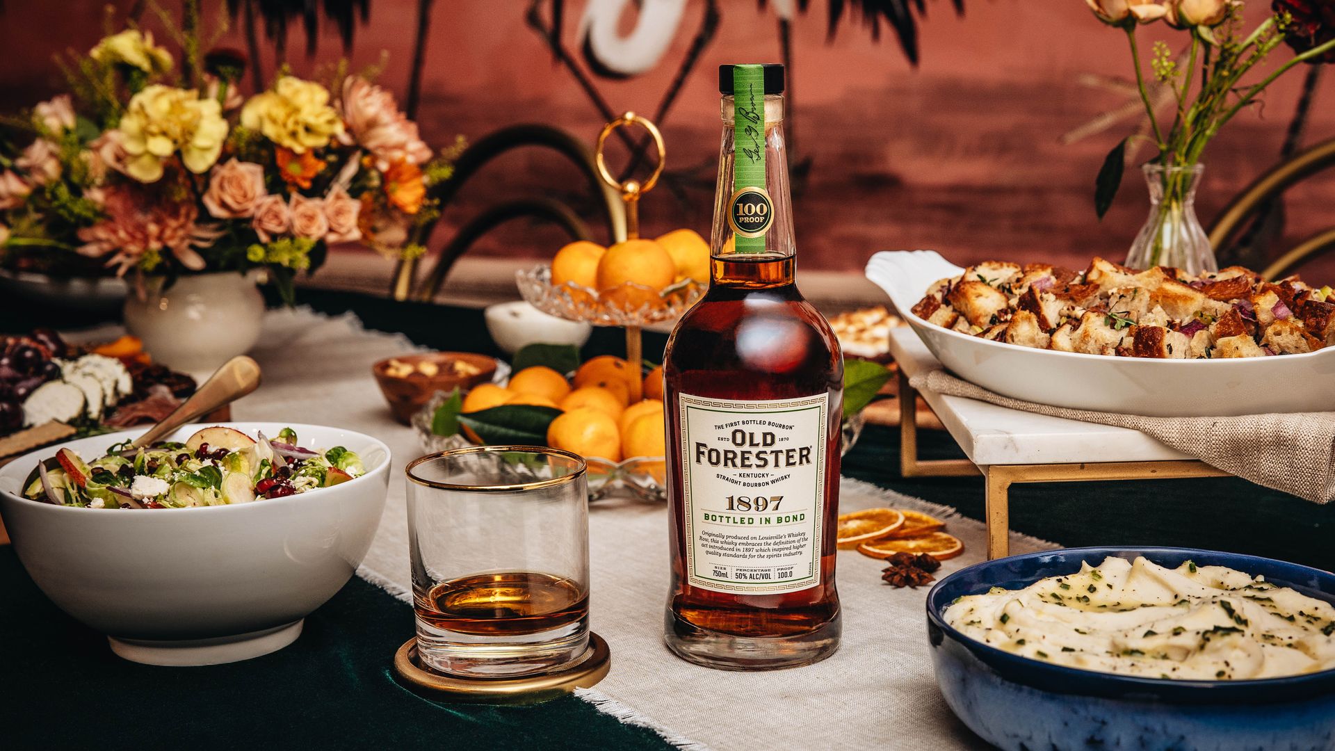 A table of food and a bottle and glass of Old Forester whiskey. 
