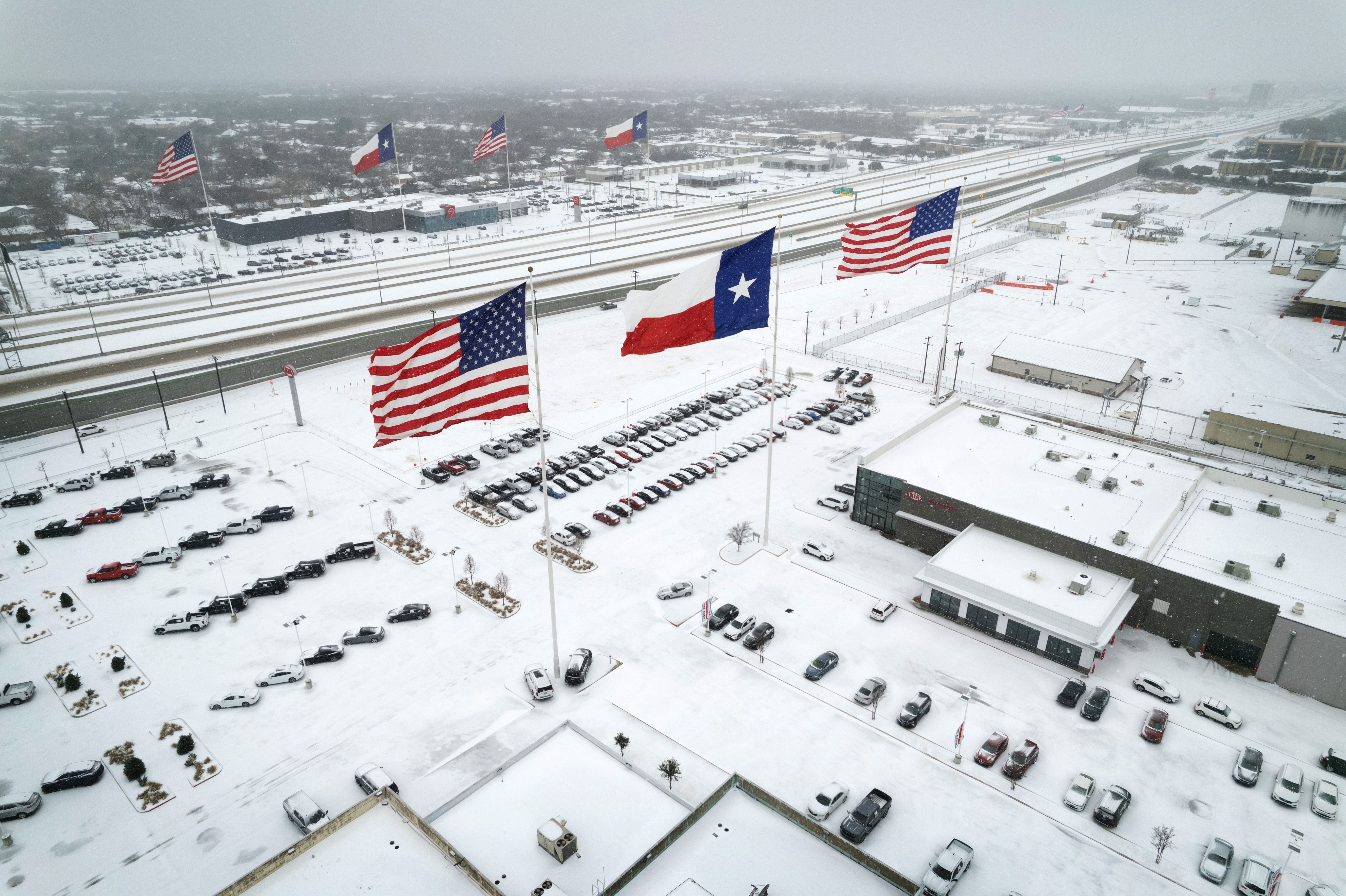 In an aerial view, U.S. and Texas state flags fly over car dealerships covered in snow