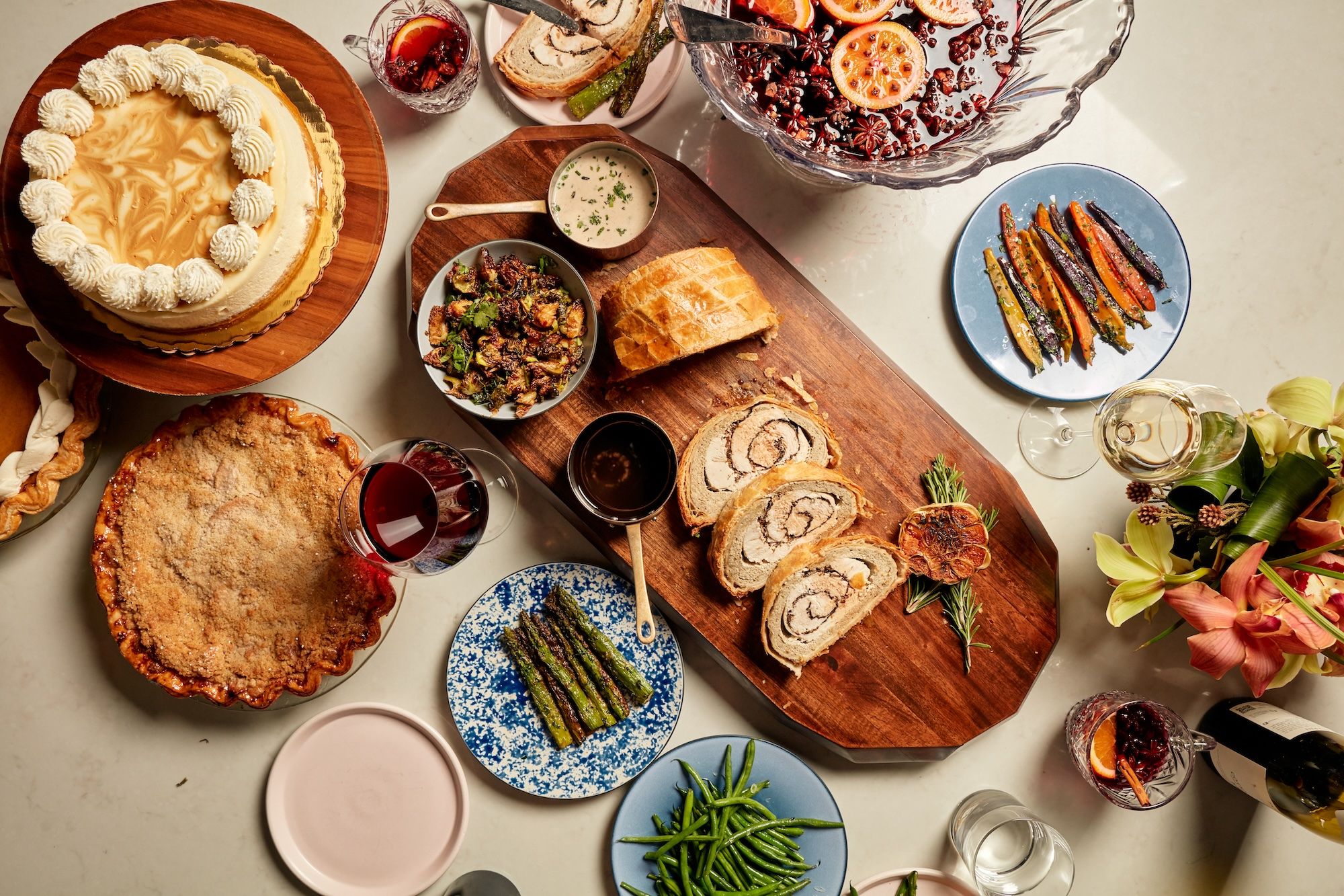 Cake, pie, glasses of wine around a cutting board with sliced turkey.