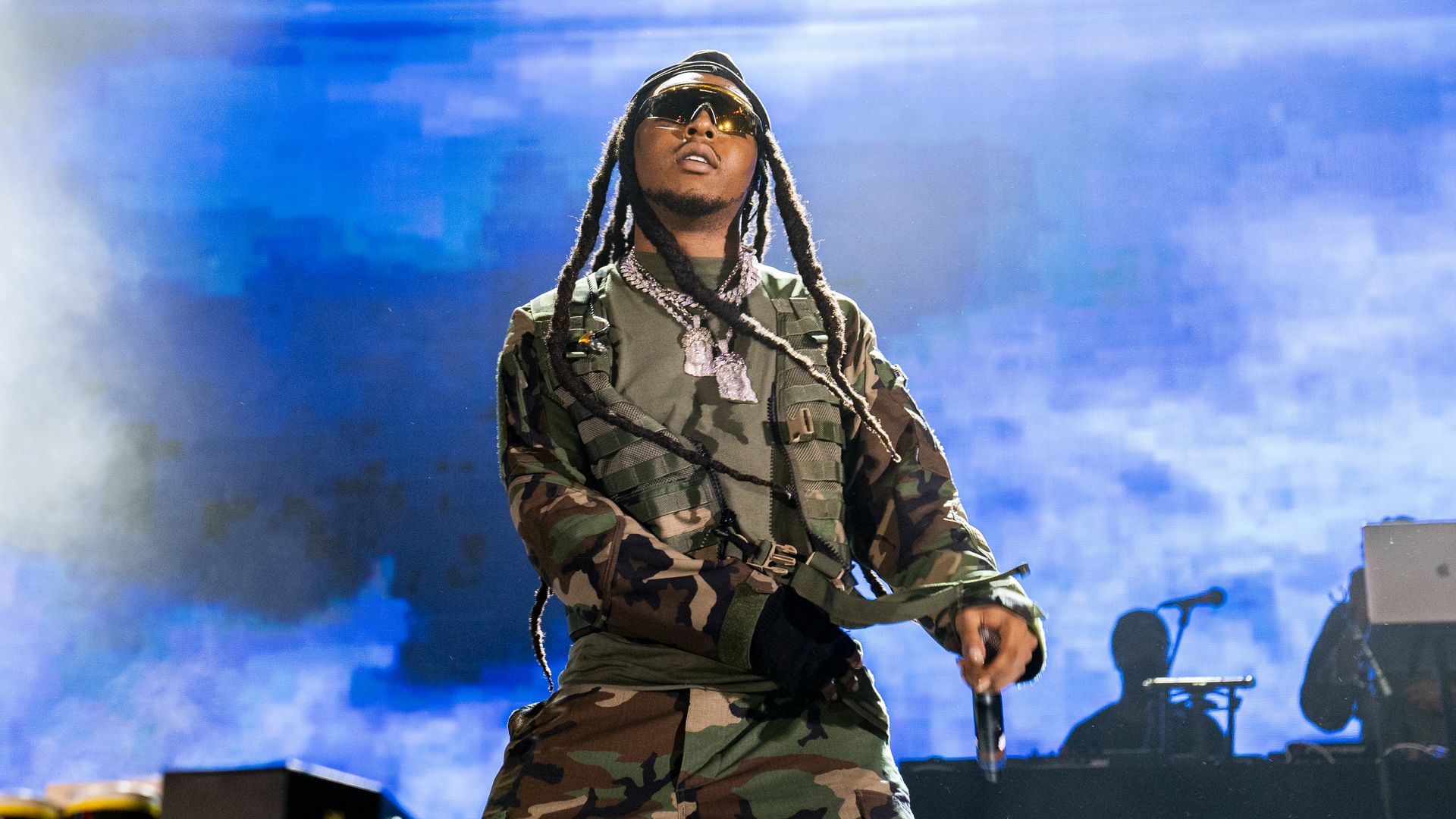 Rapper Takeoff performing on stage, in front of a blue screen. 