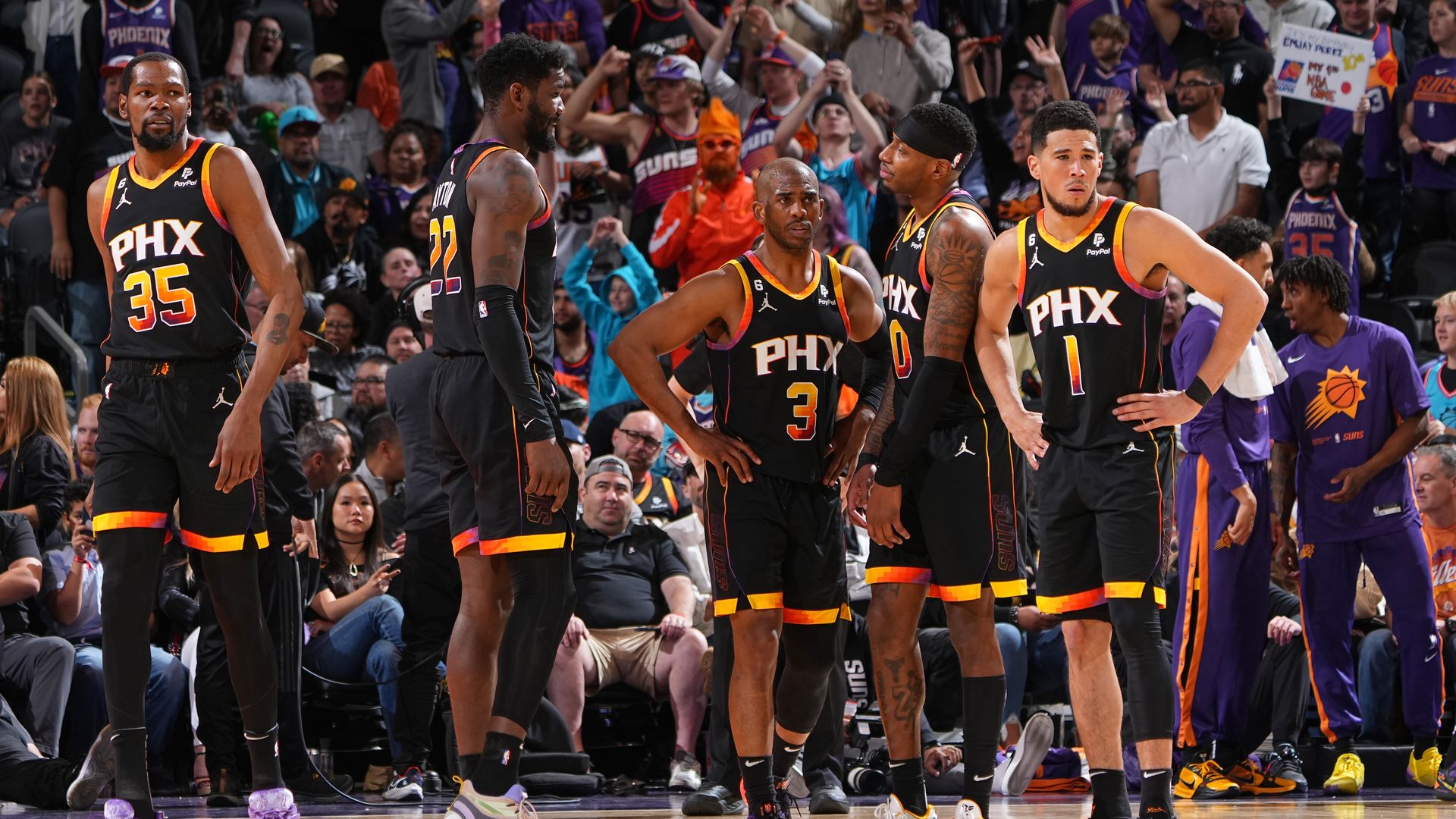 Five basketball players in black jerseys with PHX on the front stand next to each other on a basketball court.