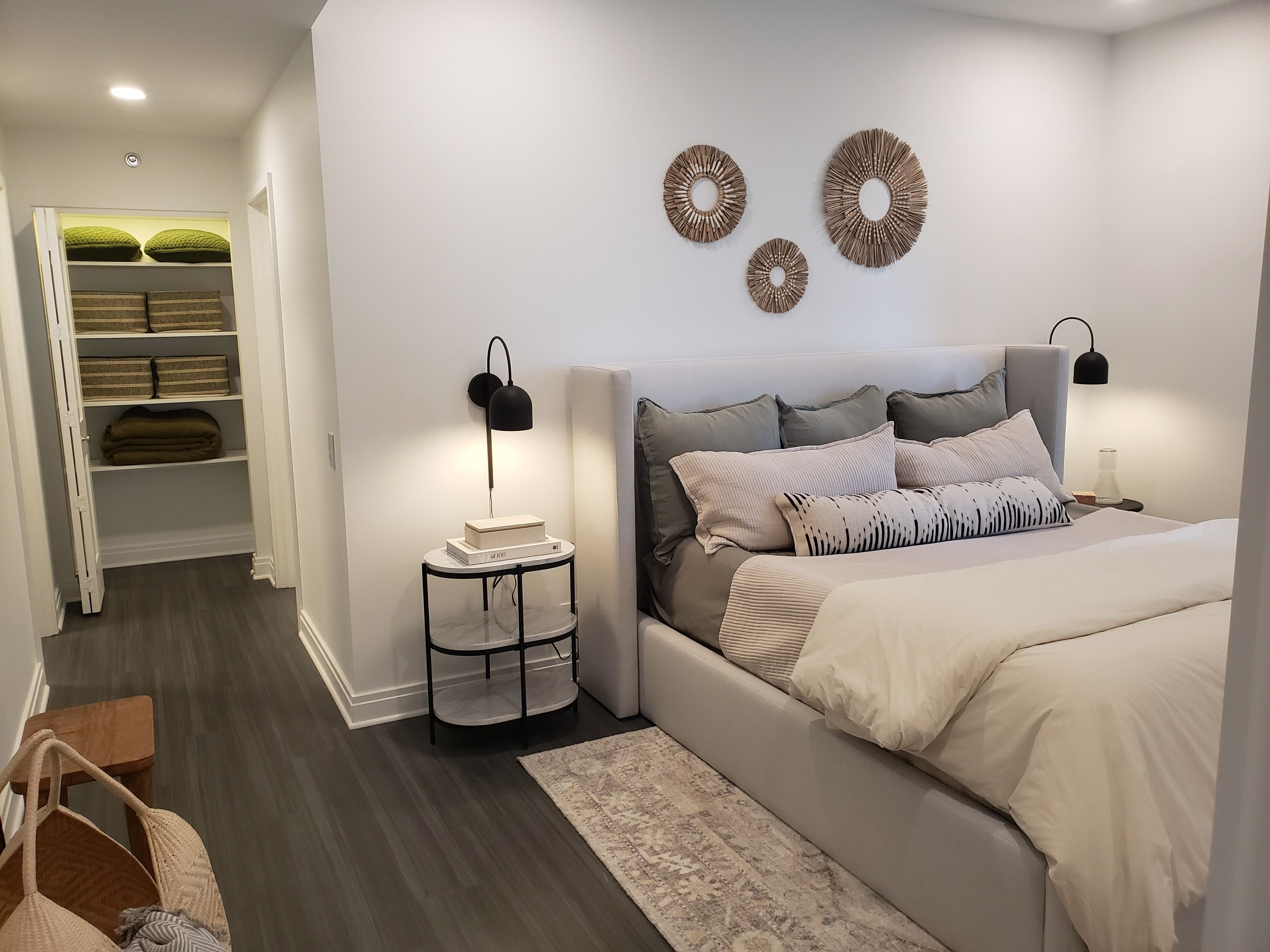 A queen grey bed is centered on a colorful rug, with a view of the closet space in a new unit at the Belden-Stratford.